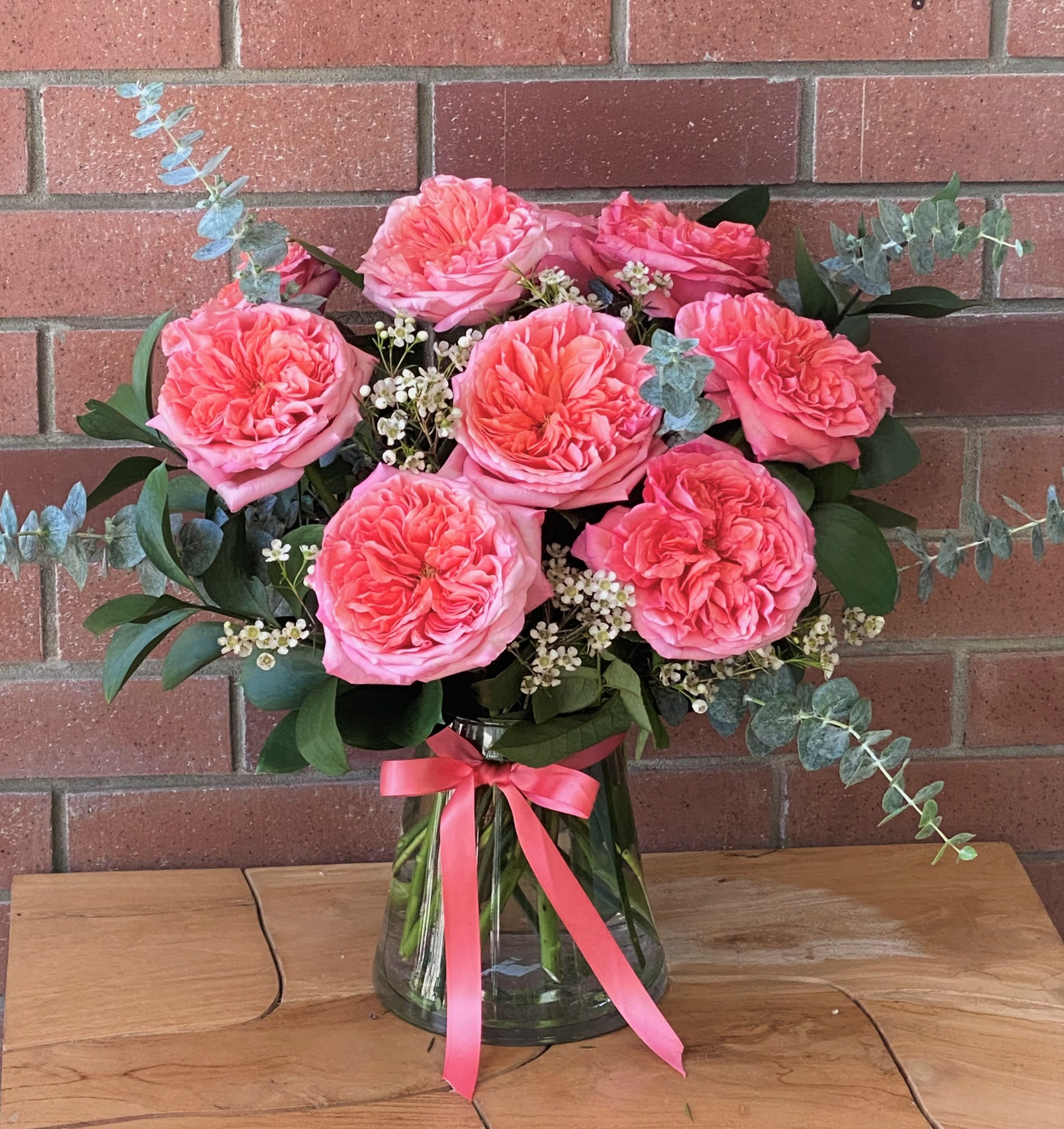 Pink roses in a glass vase with eucalyptus and a pink ribbon