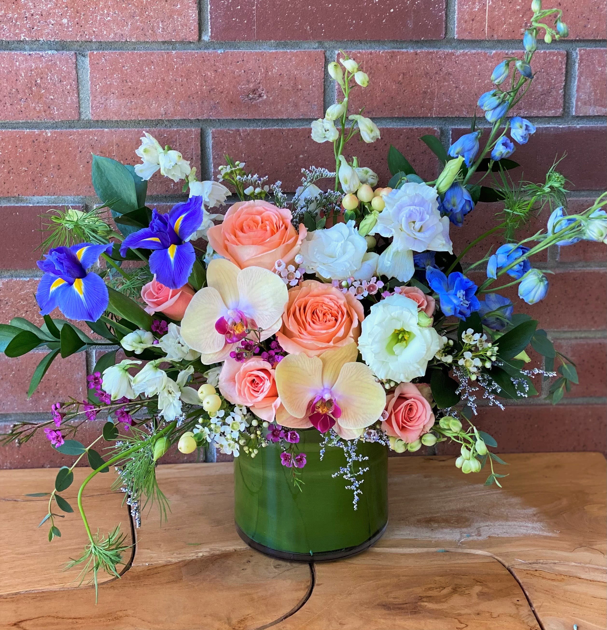 Mixed bouquet in a green glass vase with peach roses and blue irises