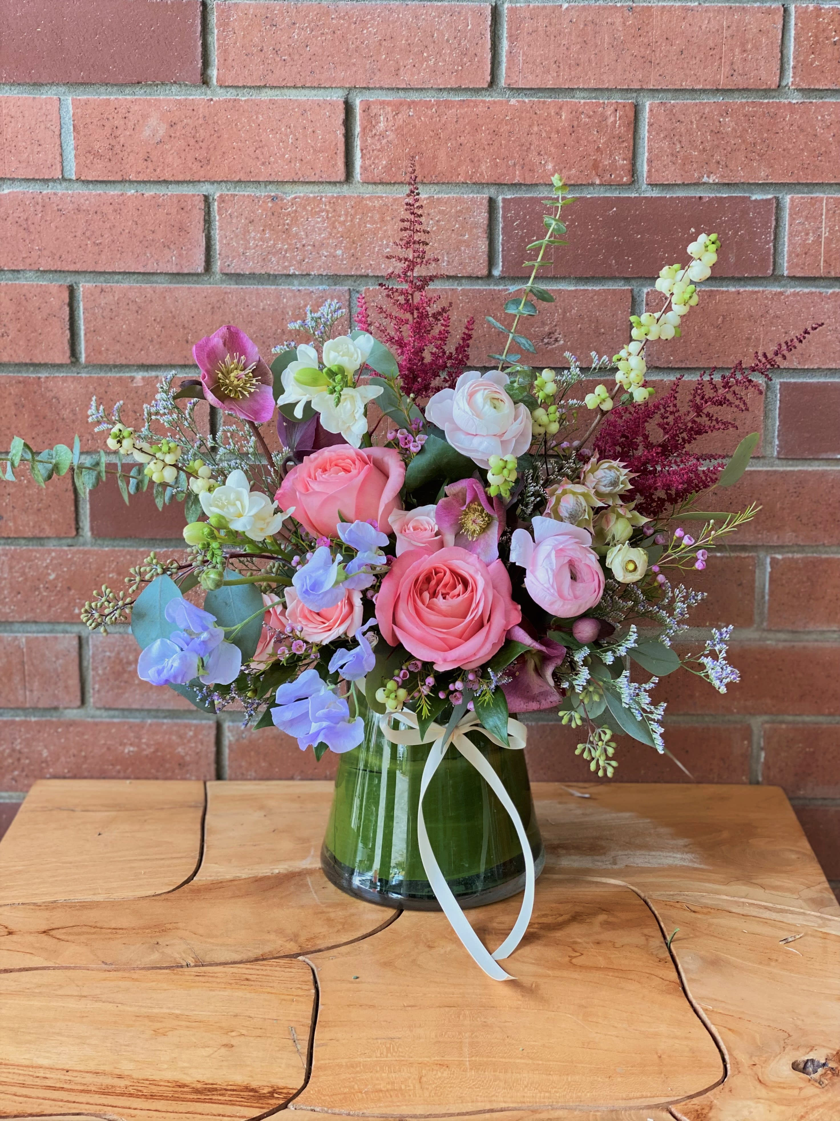 Pink and white floral arrangement in a glass vase with a ribbon