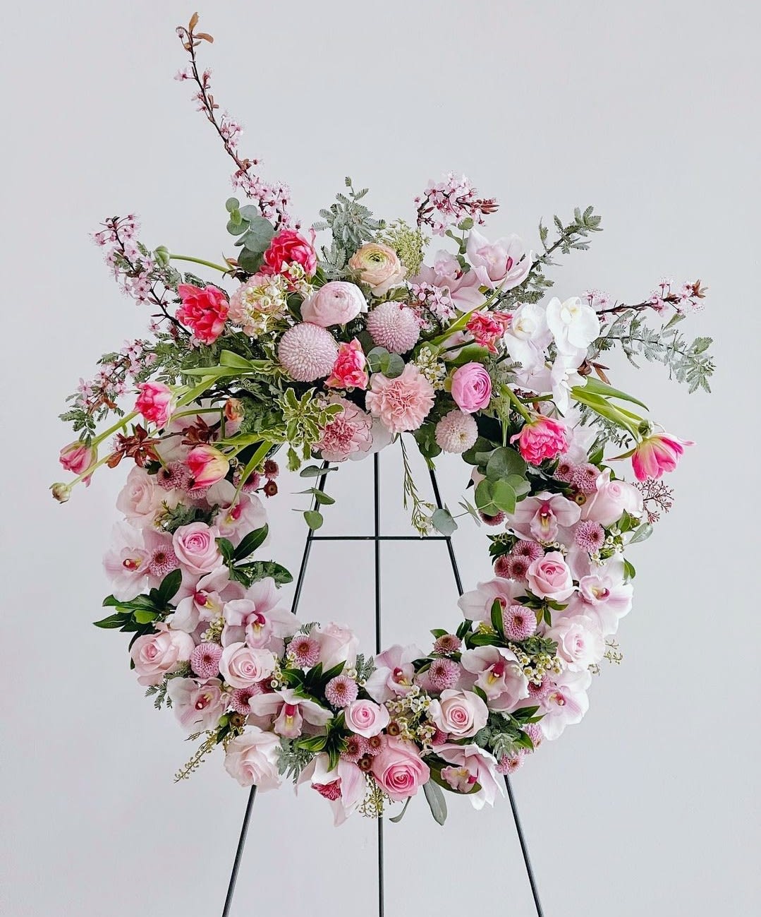 Pink floral wreath on a black stand with roses and orchids