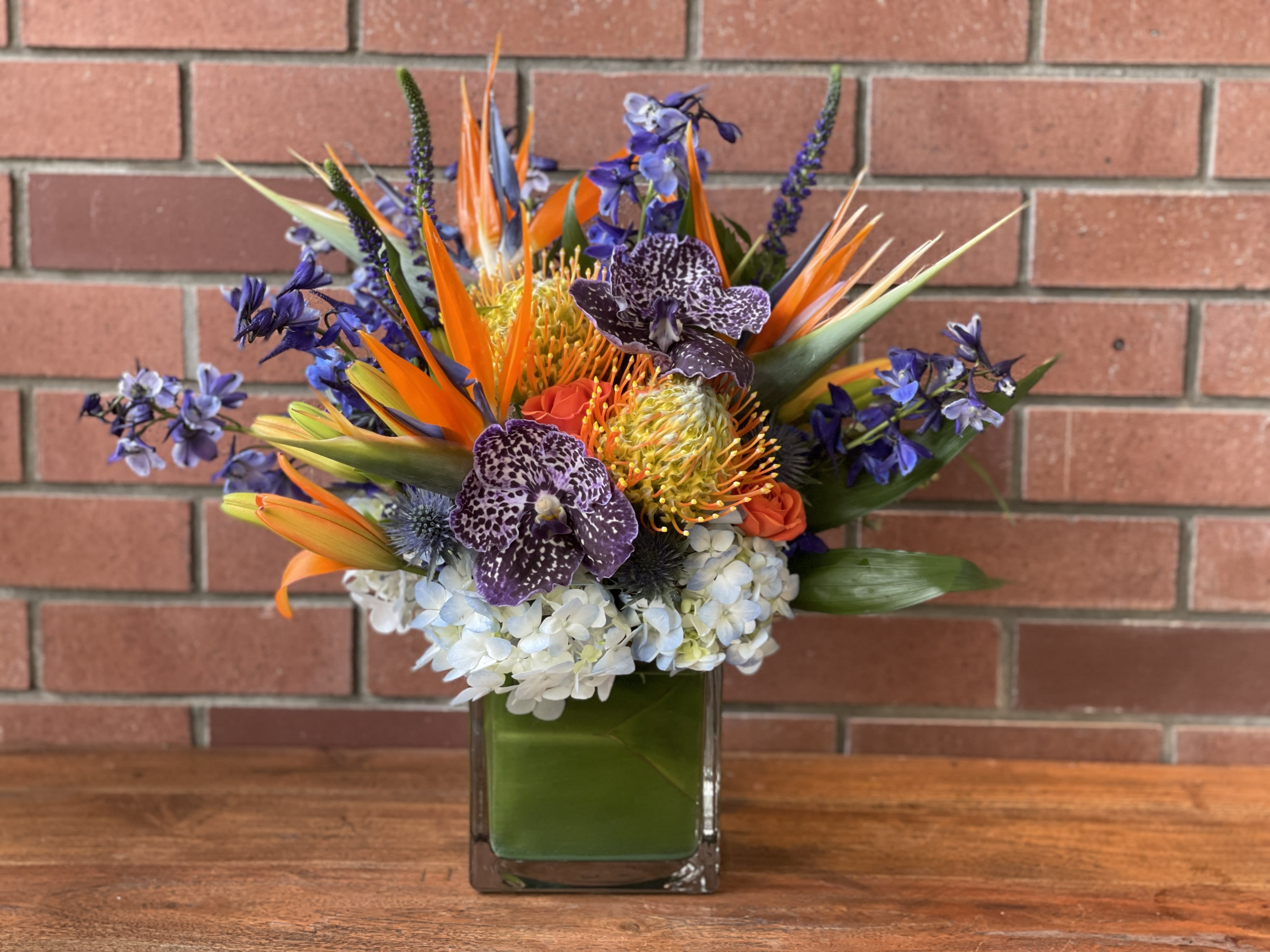 Tropical bouquet in a square glass vase with orange and purple flowers
