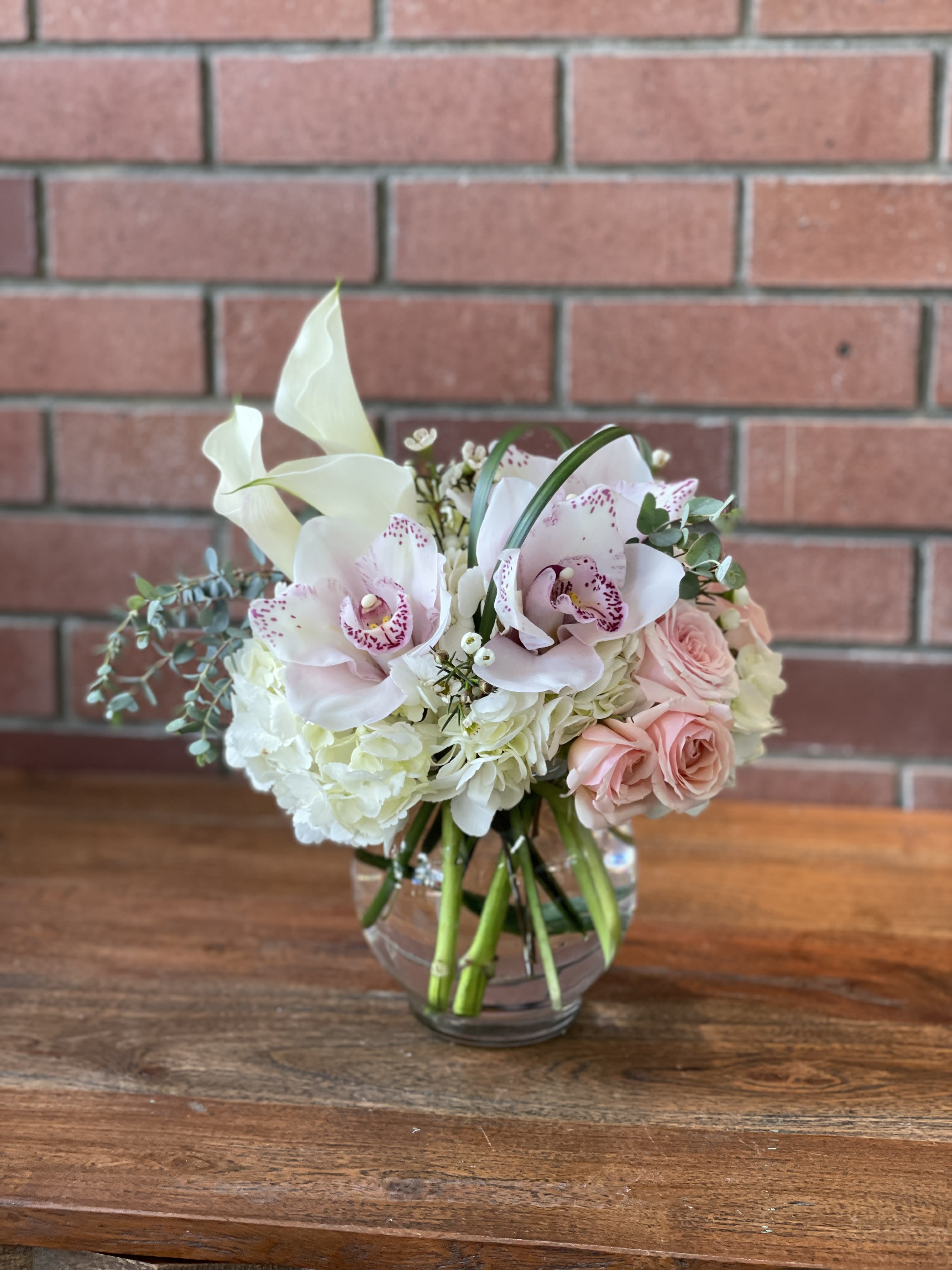 Bouquet of white orchids, pale pink roses, and white hydrangeas in a glass vase