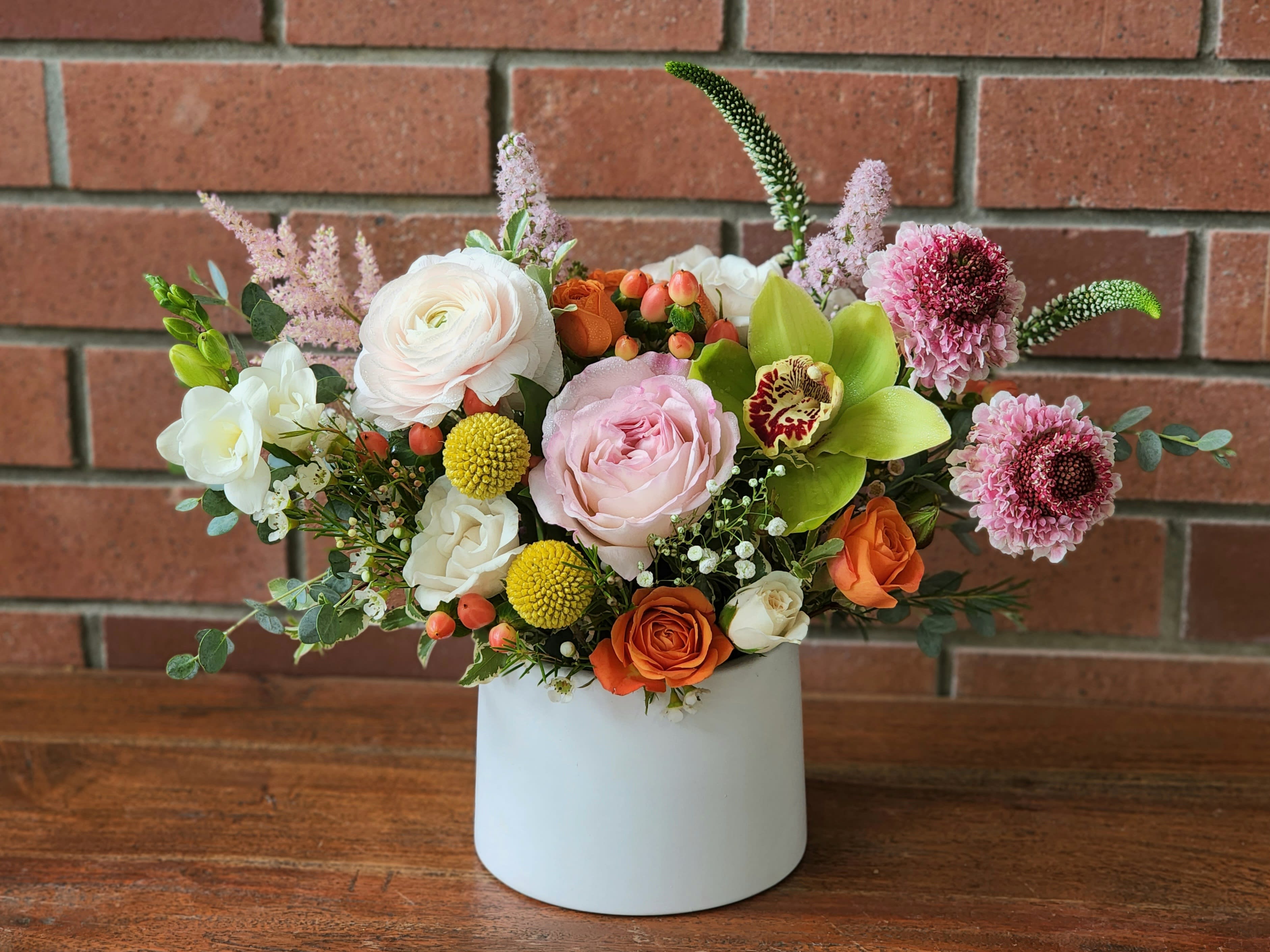 Mixed floral arrangement in a white vase with pink, white, orange, and green blooms