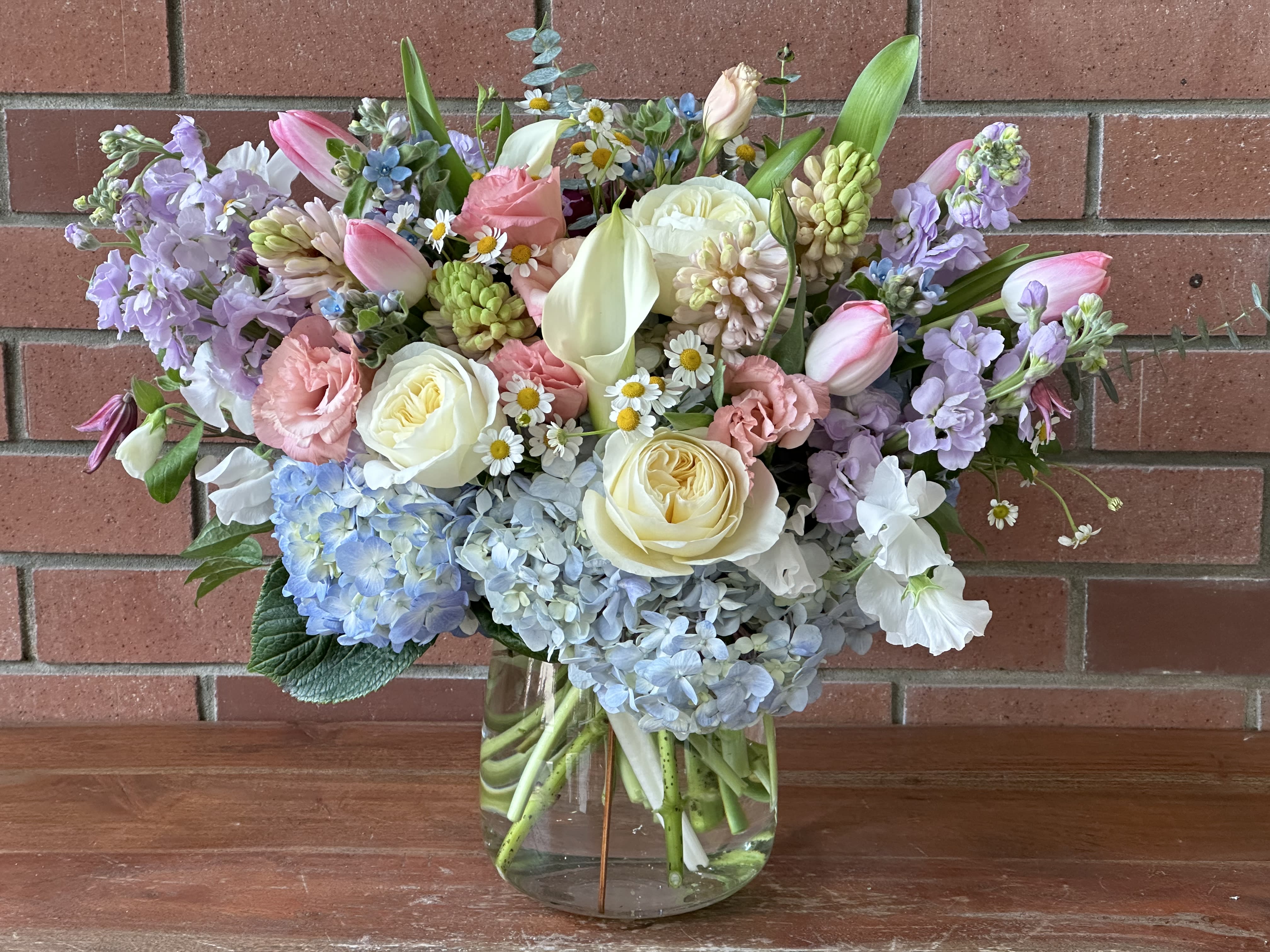 Pastel bouquet of roses, tulips, hydrangeas, and lilies in a glass vase