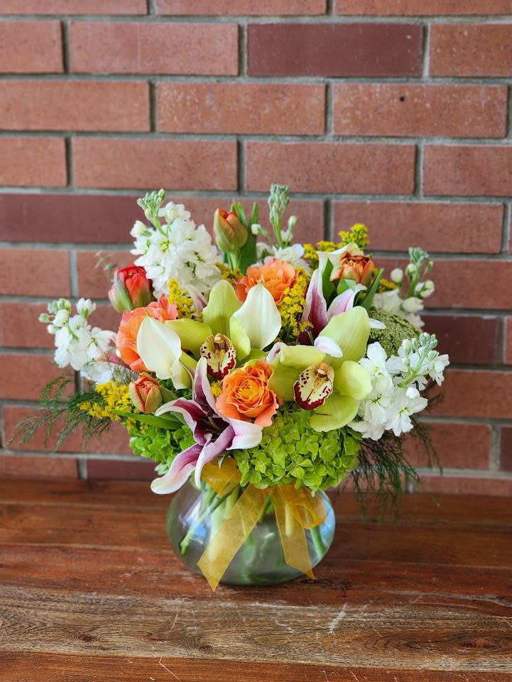 Mixed bouquet in a glass vase with orange roses, orchids, and white blooms
