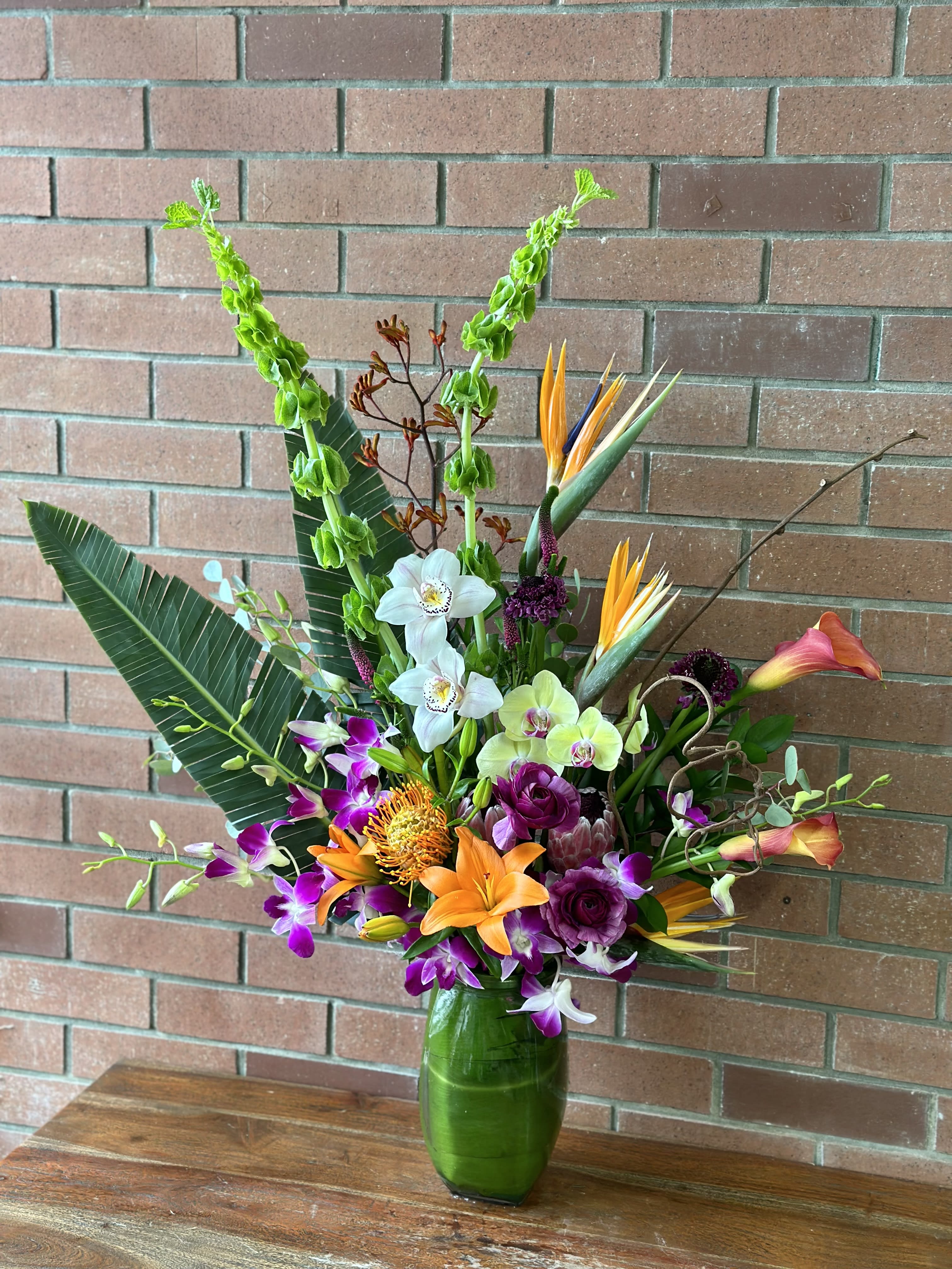 Tropical flower arrangement in a green glass vase with orchids and lilies