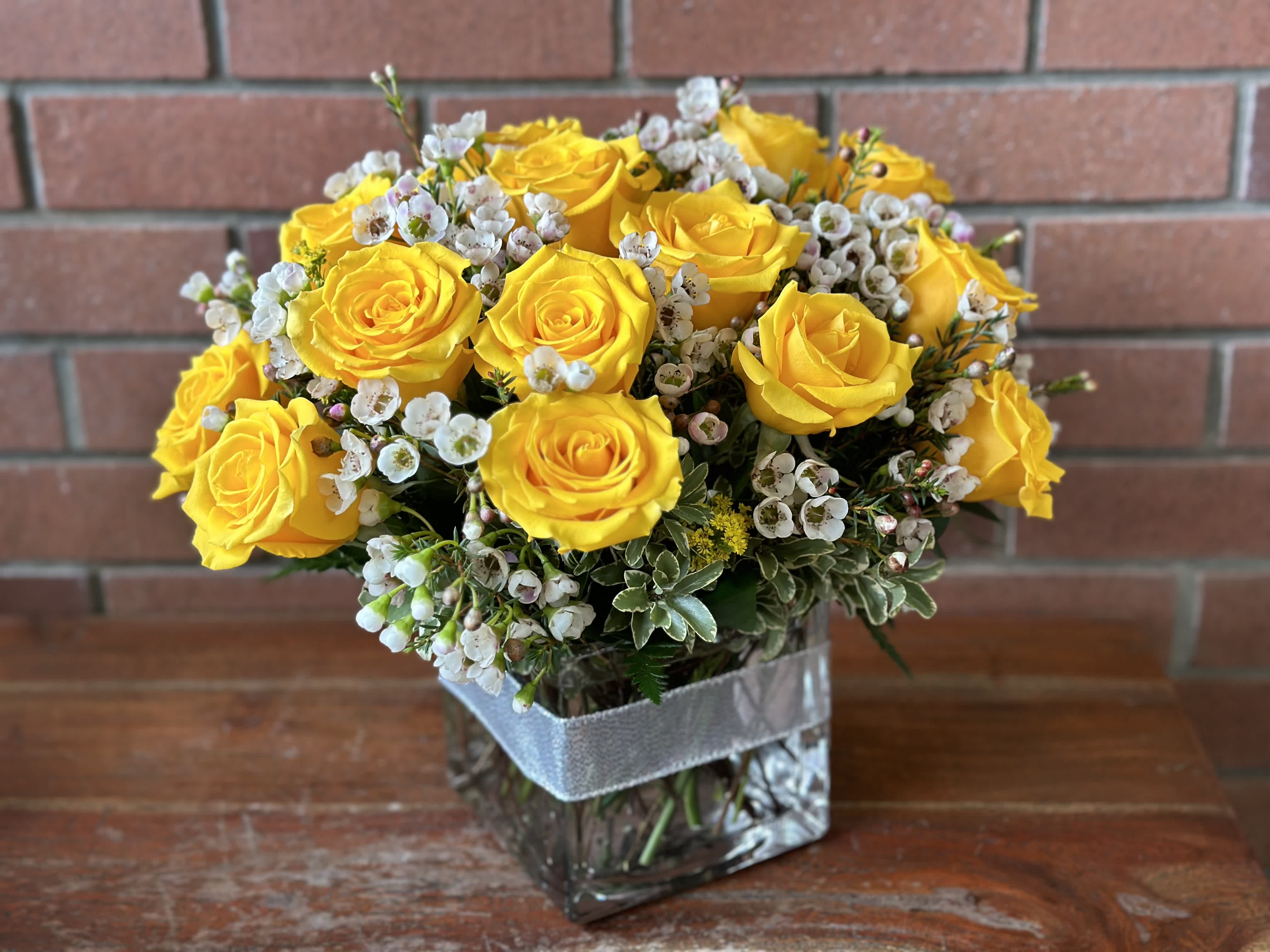 Yellow roses arranged in a square glass vase with small white filler flowers