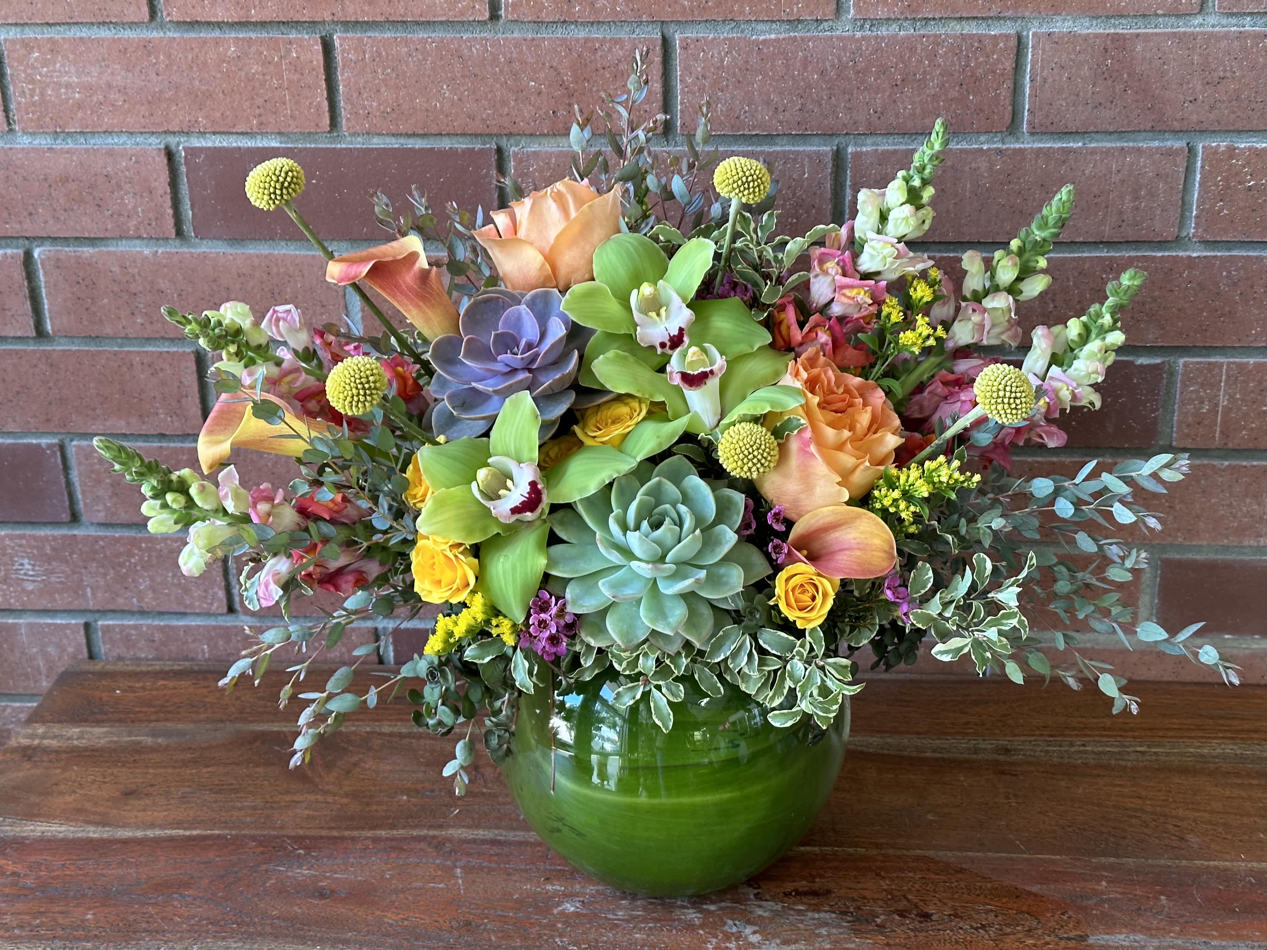 Mixed floral arrangement in a green glass vase with succulents and orchids