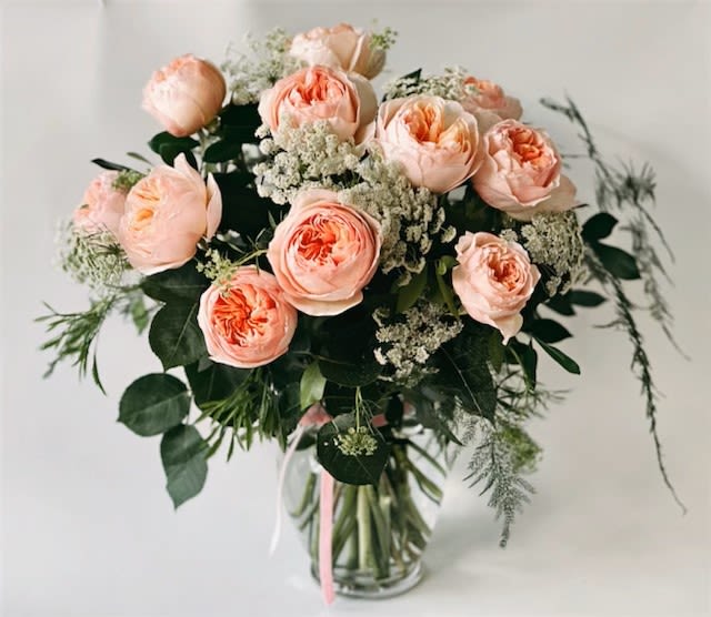 Peach garden roses and white filler flowers arranged in a clear glass vase