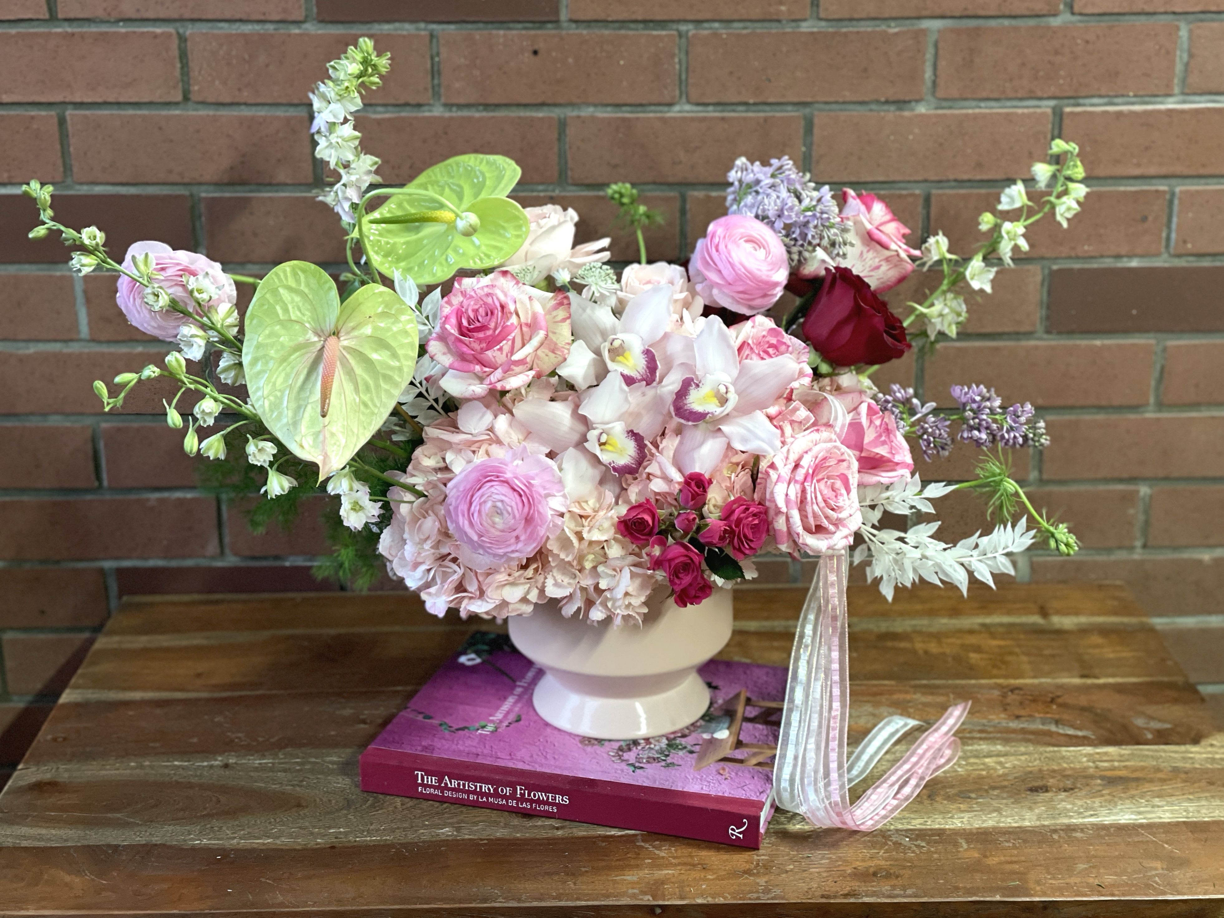 Pink and white floral arrangement in a white vase with ribbon