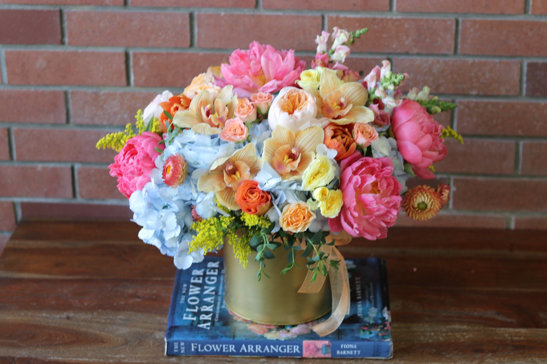 Colorful mixed flower arrangement in a gold vase on stacked books