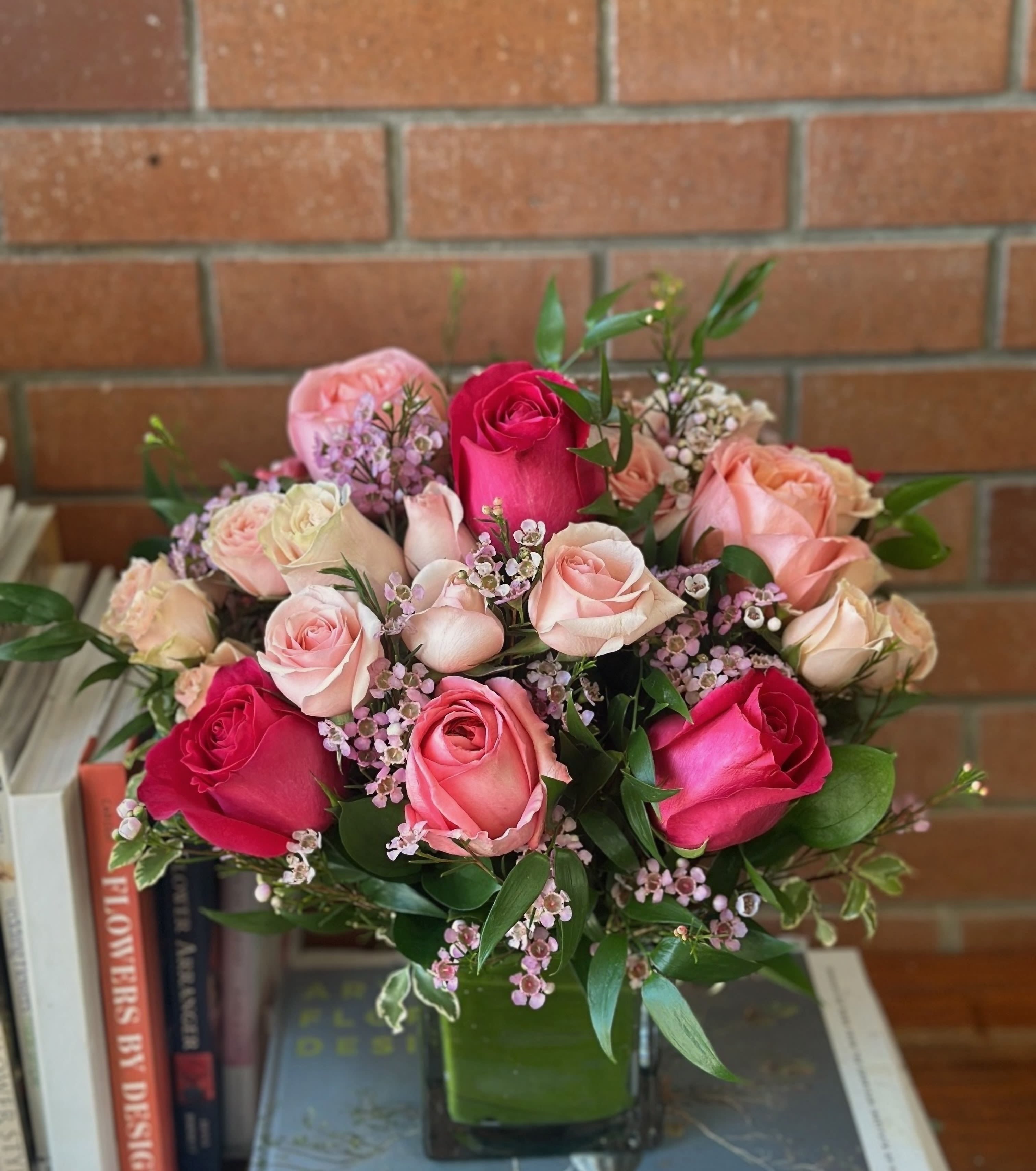 Rounded arrangement of pink and cream roses with tiny pink blossoms in a square glass vase