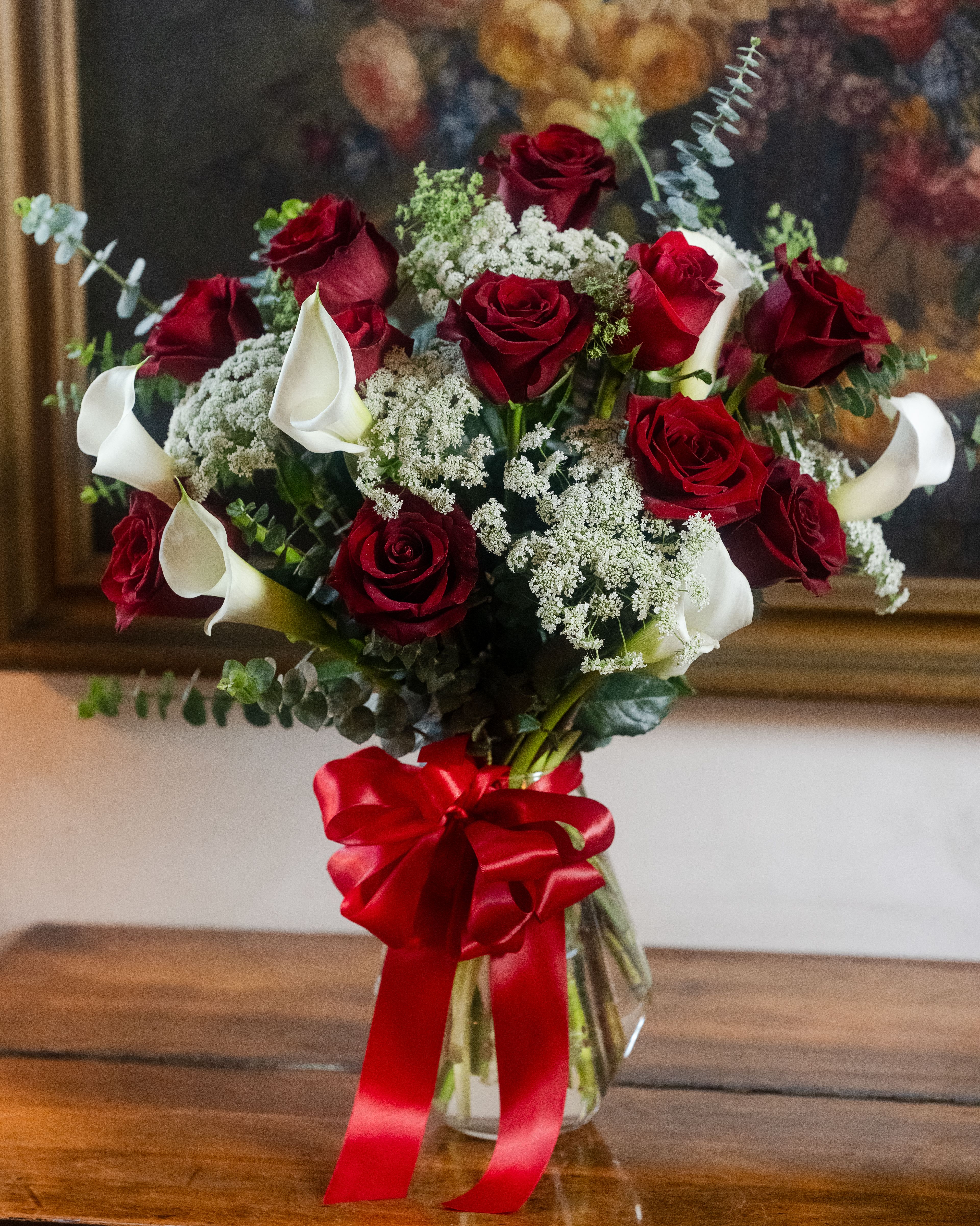 Bouquet of red roses and white calla lilies in a glass vase with a red ribbon