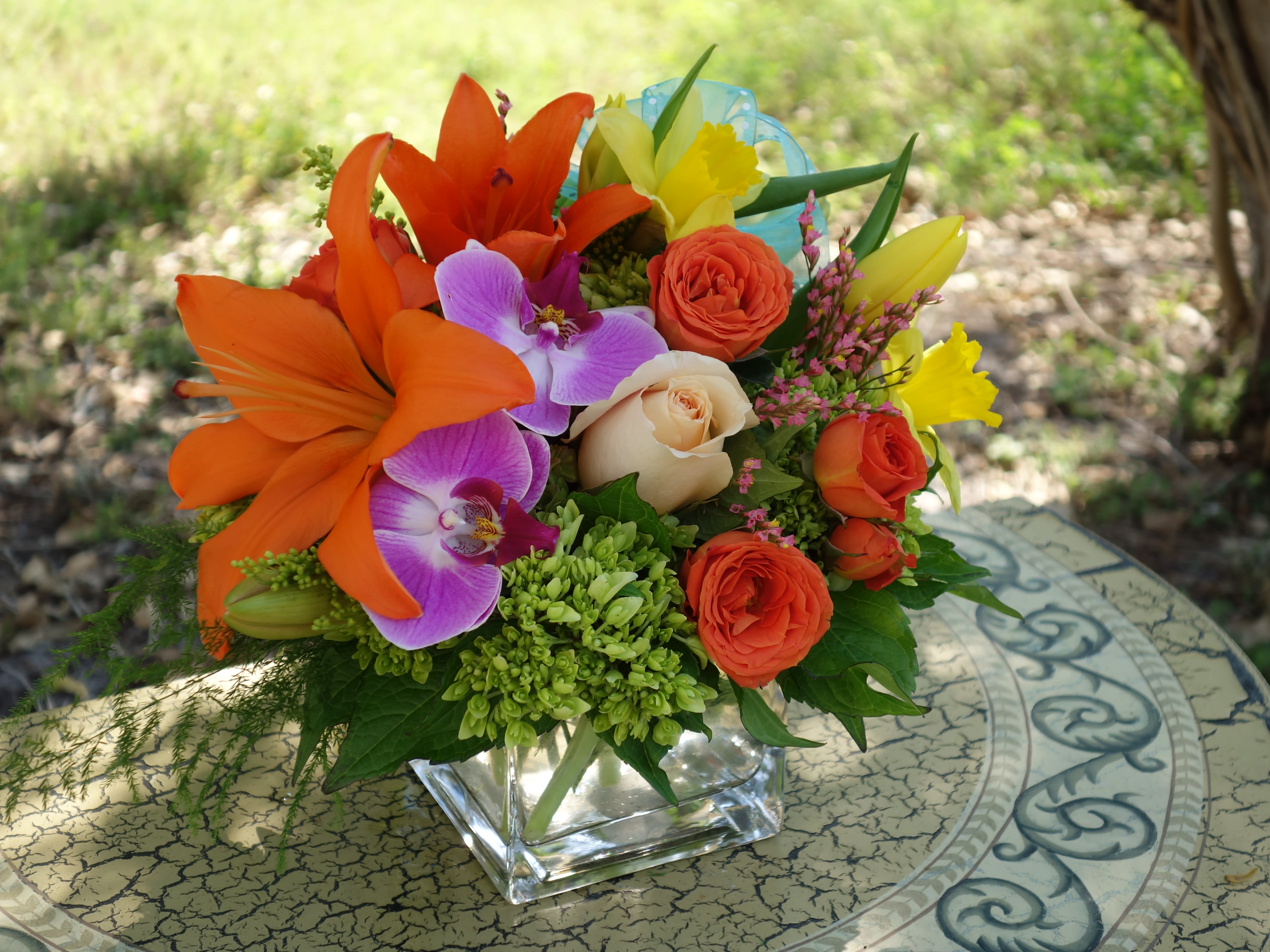 Bright mixed bouquet with orange lilies, roses, and purple orchids in a glass vase