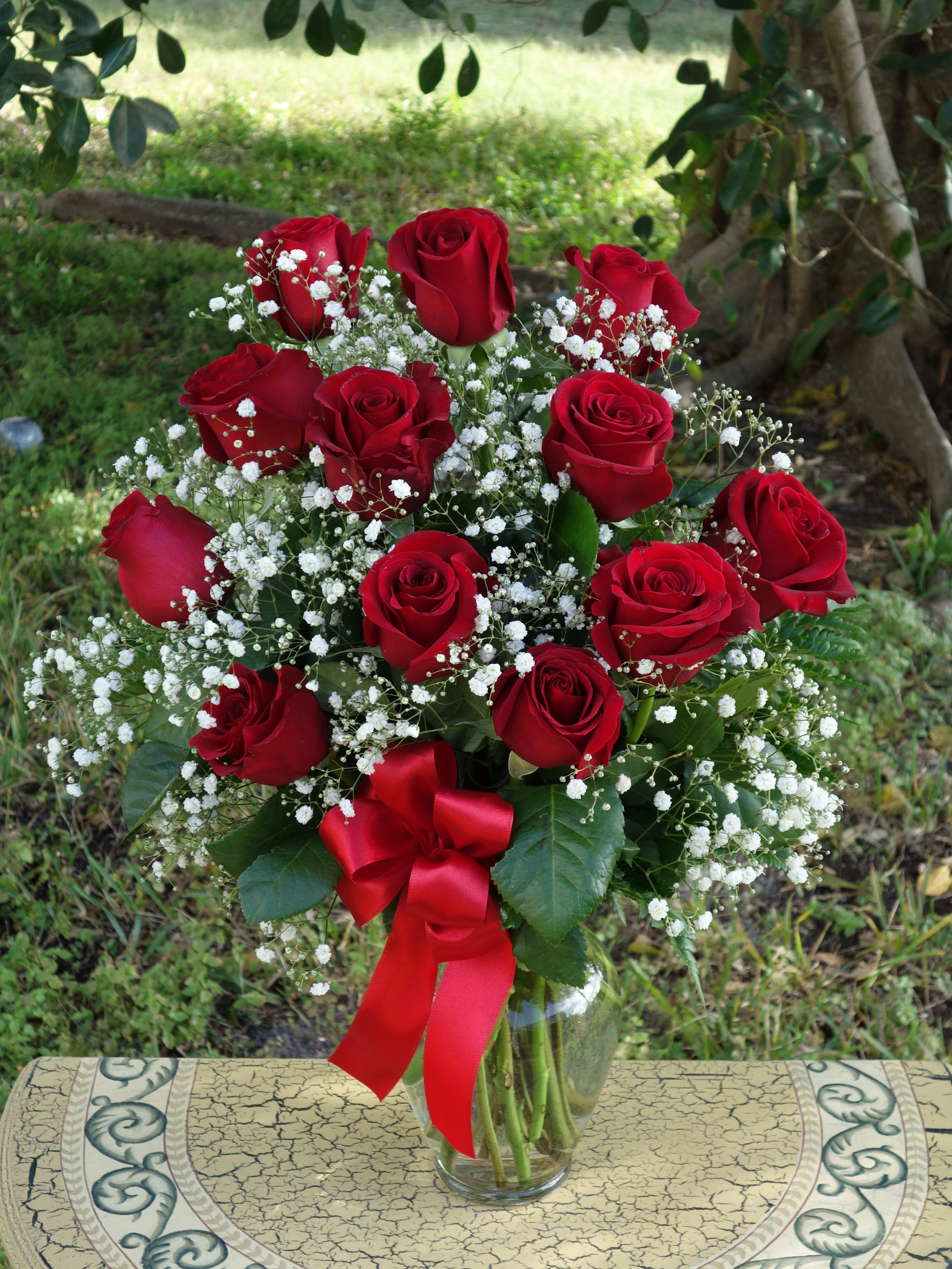 Vase of red roses with white filler flowers and a red satin bow
