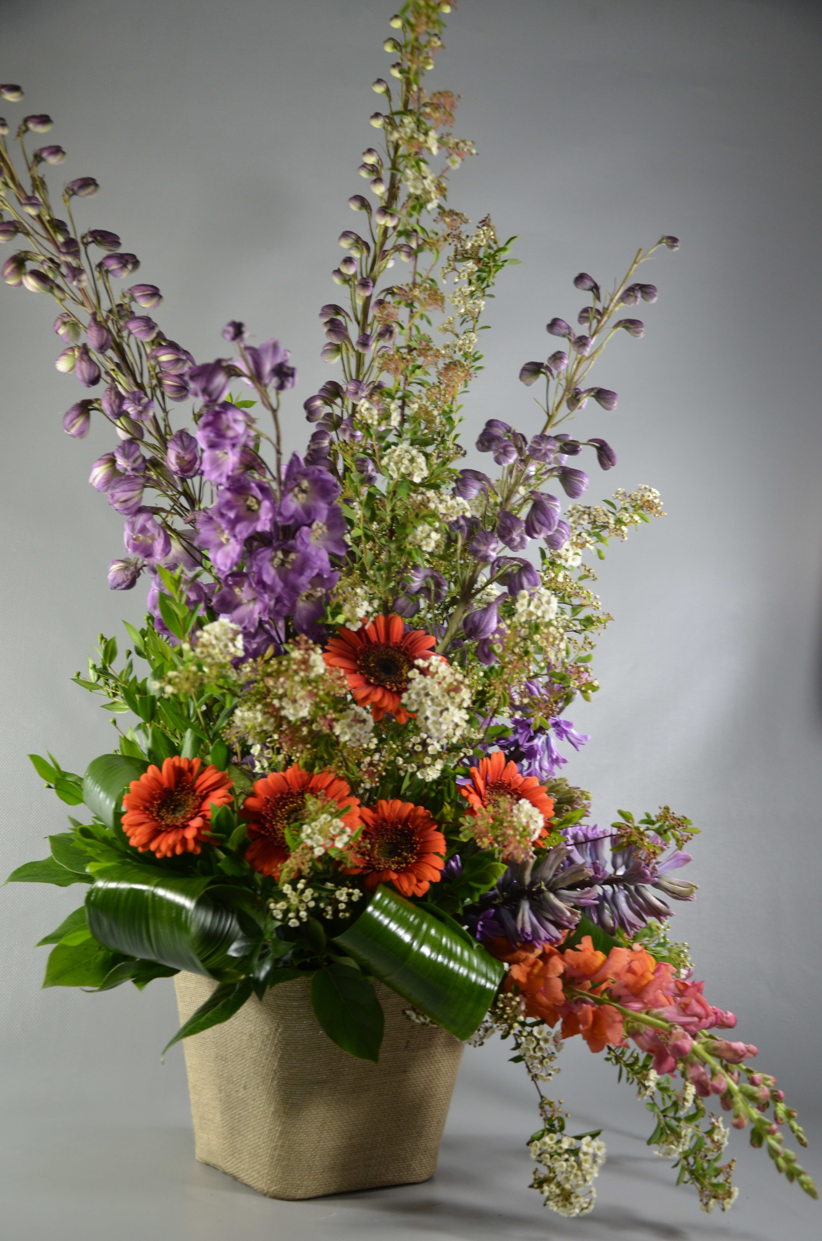 Tall mixed flower arrangement in a woven basket with orange and purple blooms