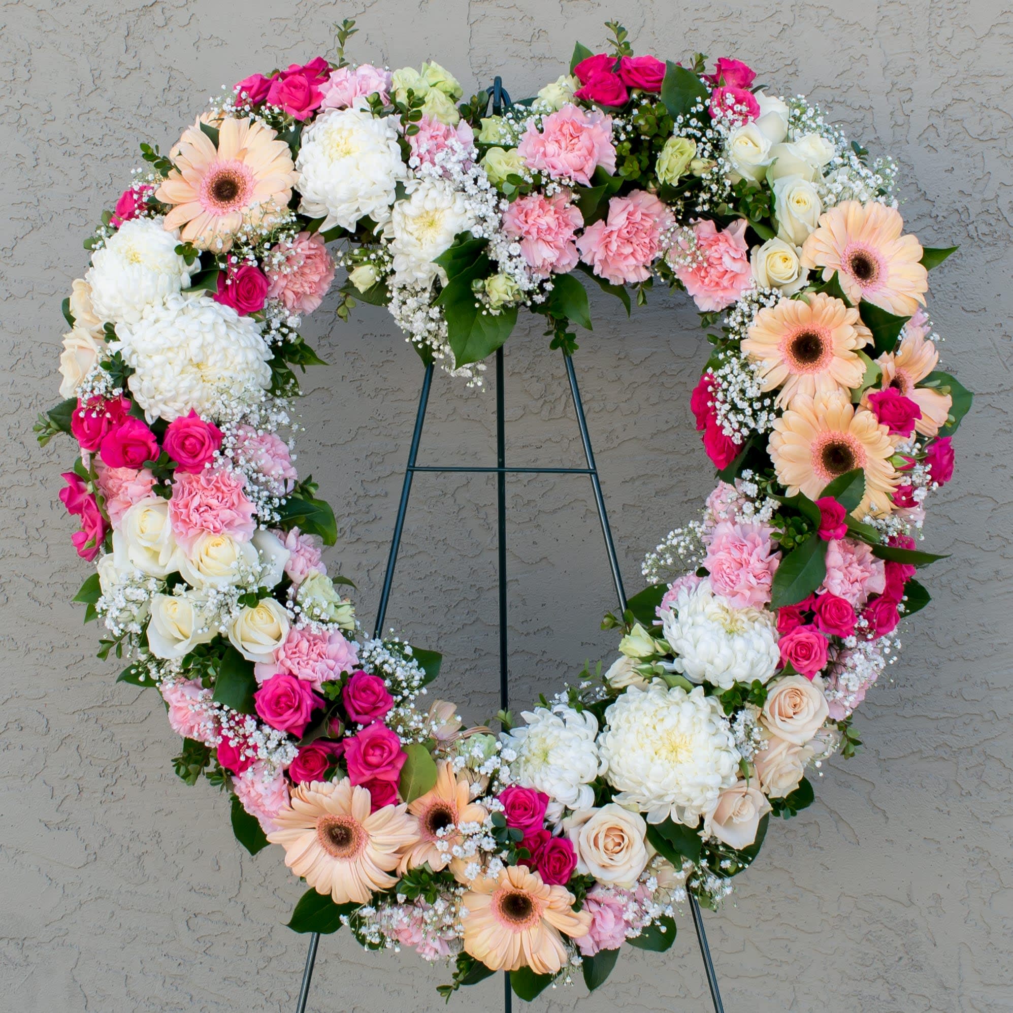 Heart-shaped floral wreath with pink, white, and peach flowers on a stand