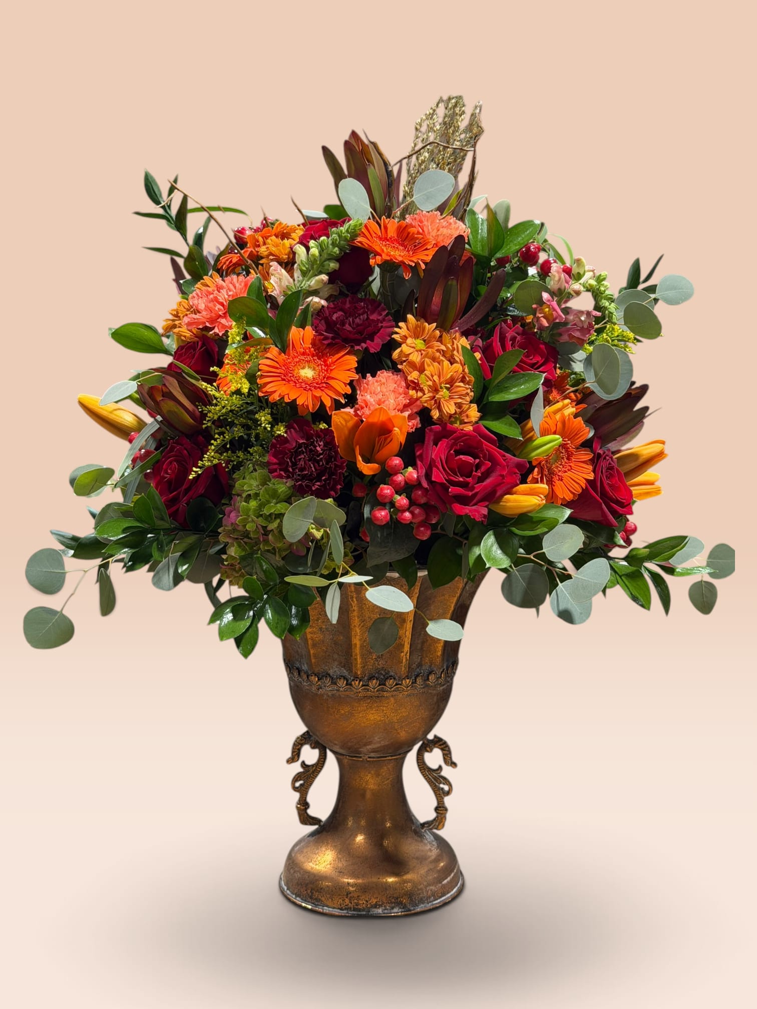 Mixed bouquet of orange, red, and pink flowers in a bronze urn vase