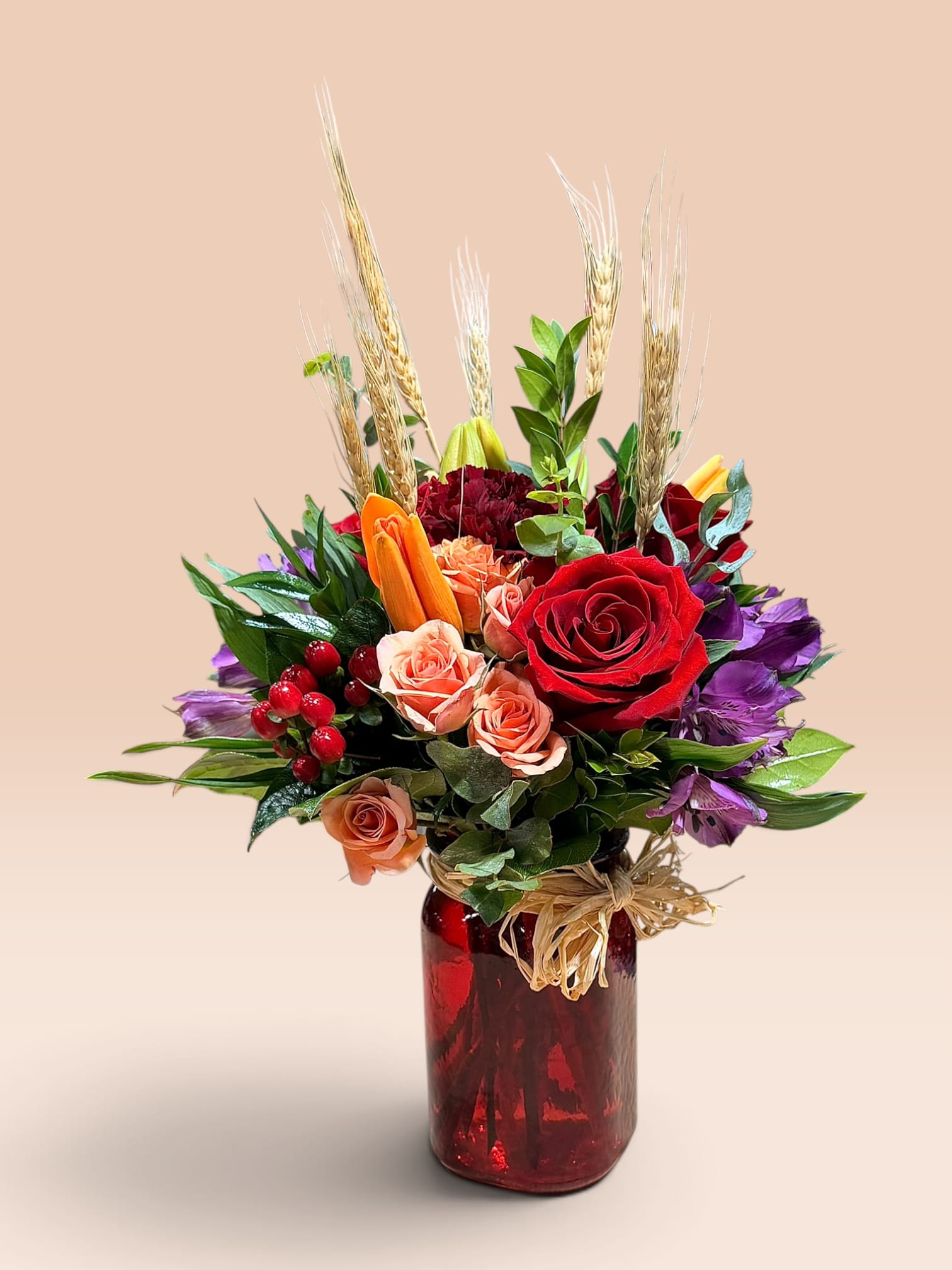 Mixed bouquet of red, peach, and purple flowers in a red glass vase