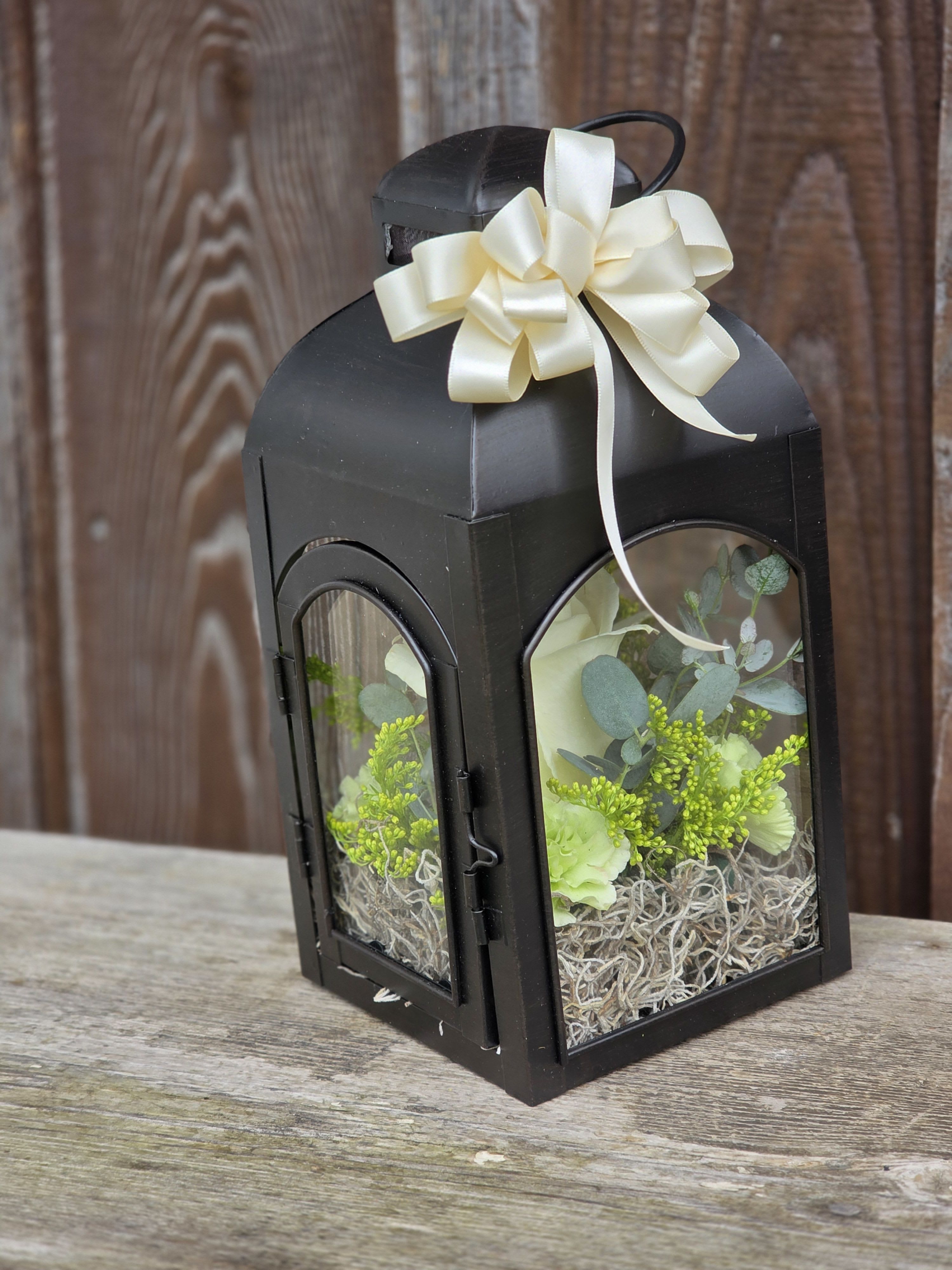 Black lantern with cream ribbon and pale flowers inside