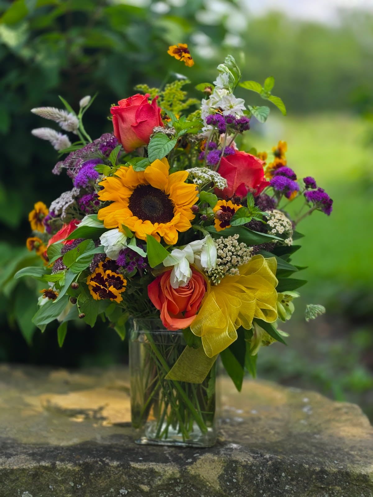 Summer Breeze - A bright and colorful mixture of beautiful summer blooms! Filled with sunflowers, roses, ageratum, gomphrena, veronica and more. This is a cheerful design that brings the beautiful bounty of summer harvest indoors. Many of these blooms are harvested right off our own flower farm!