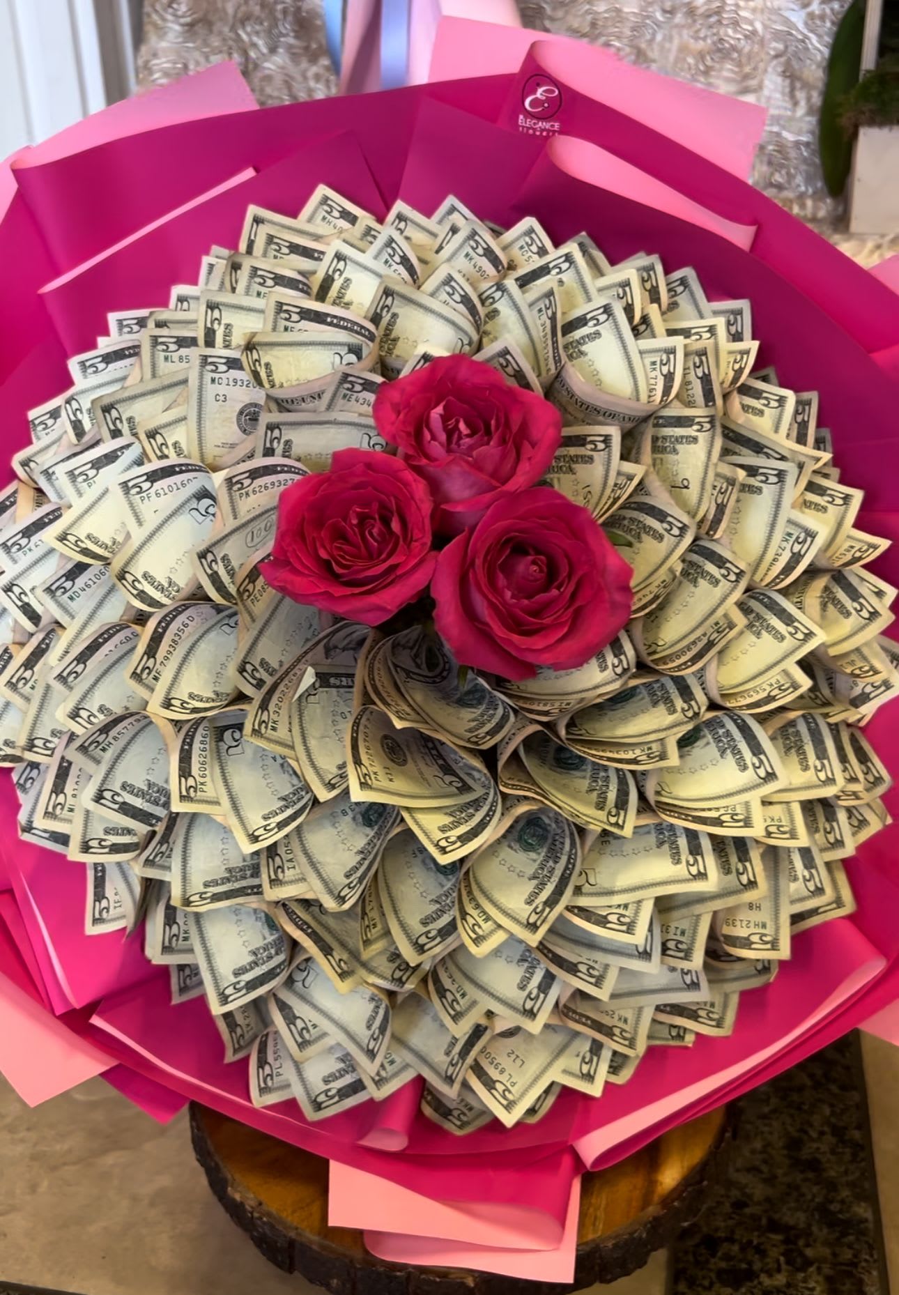 Bouquet of pink roses surrounded by folded dollar bills in bright pink wrapping
