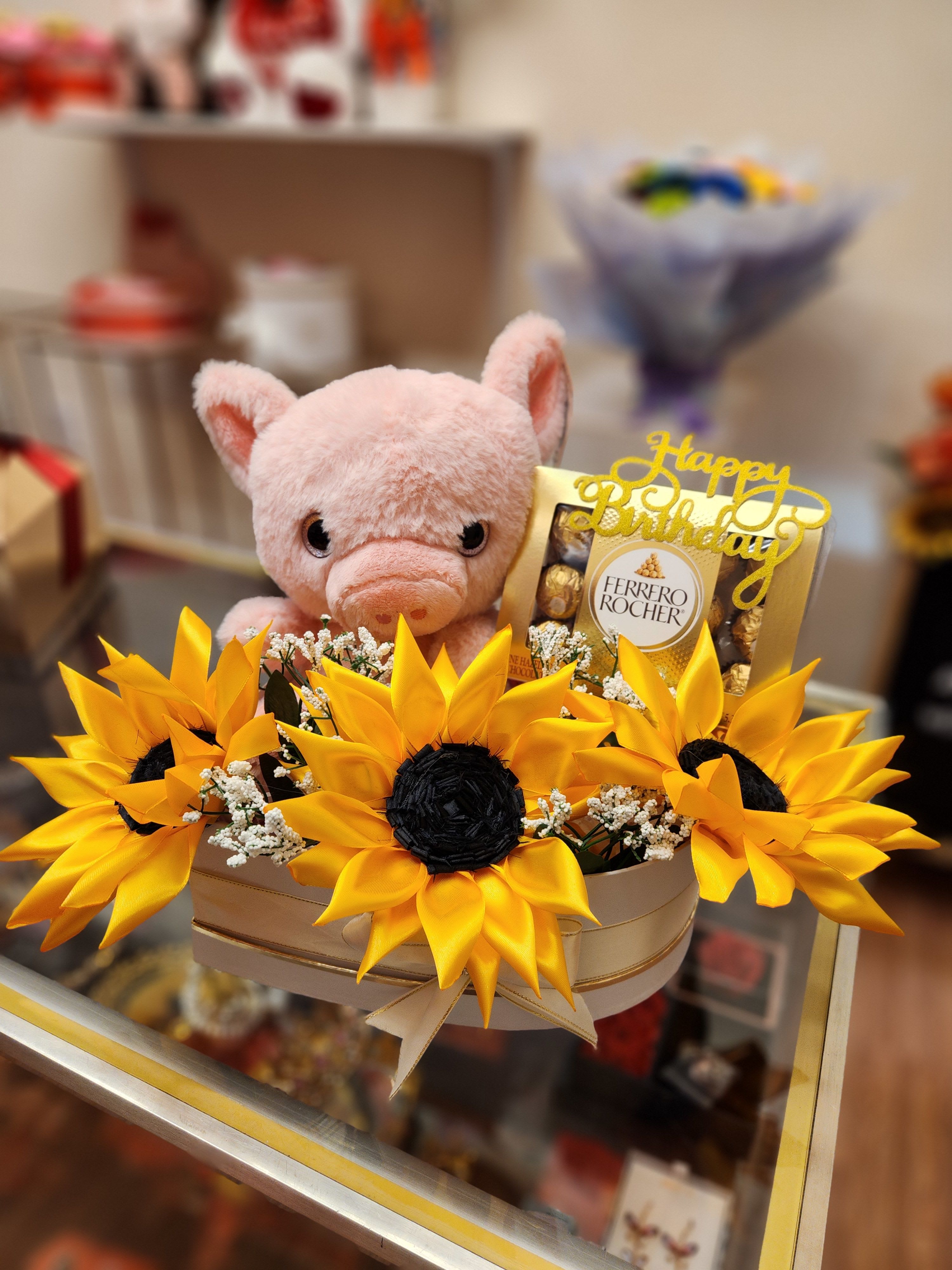 Pink plush pig in a box with yellow sunflowers and chocolates