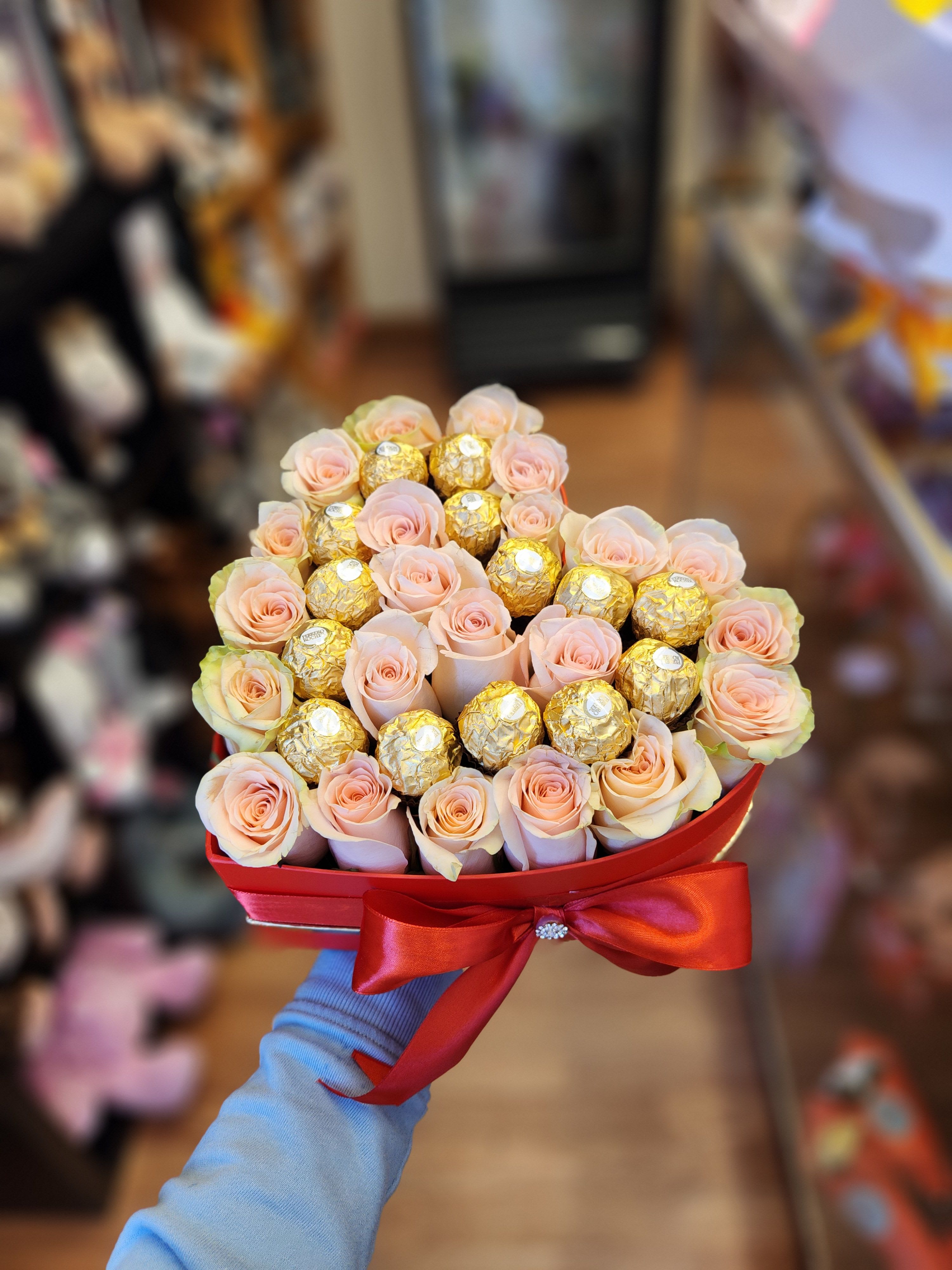 Pink roses and gold-wrapped chocolates in a red heart-shaped box with a ribbon