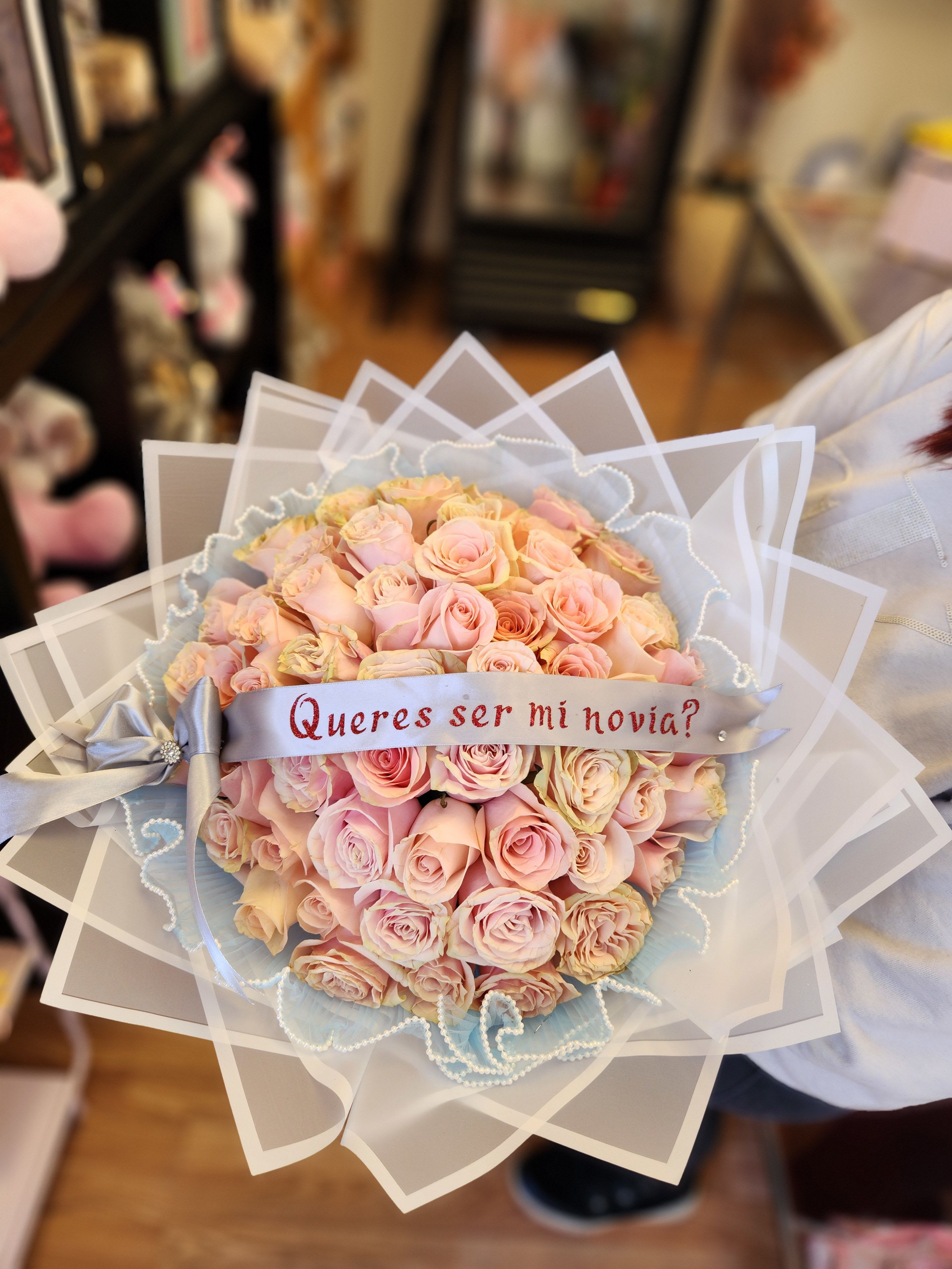 Bouquet of pale pink roses with a ribbon reading "Quieres ser mi novia?"