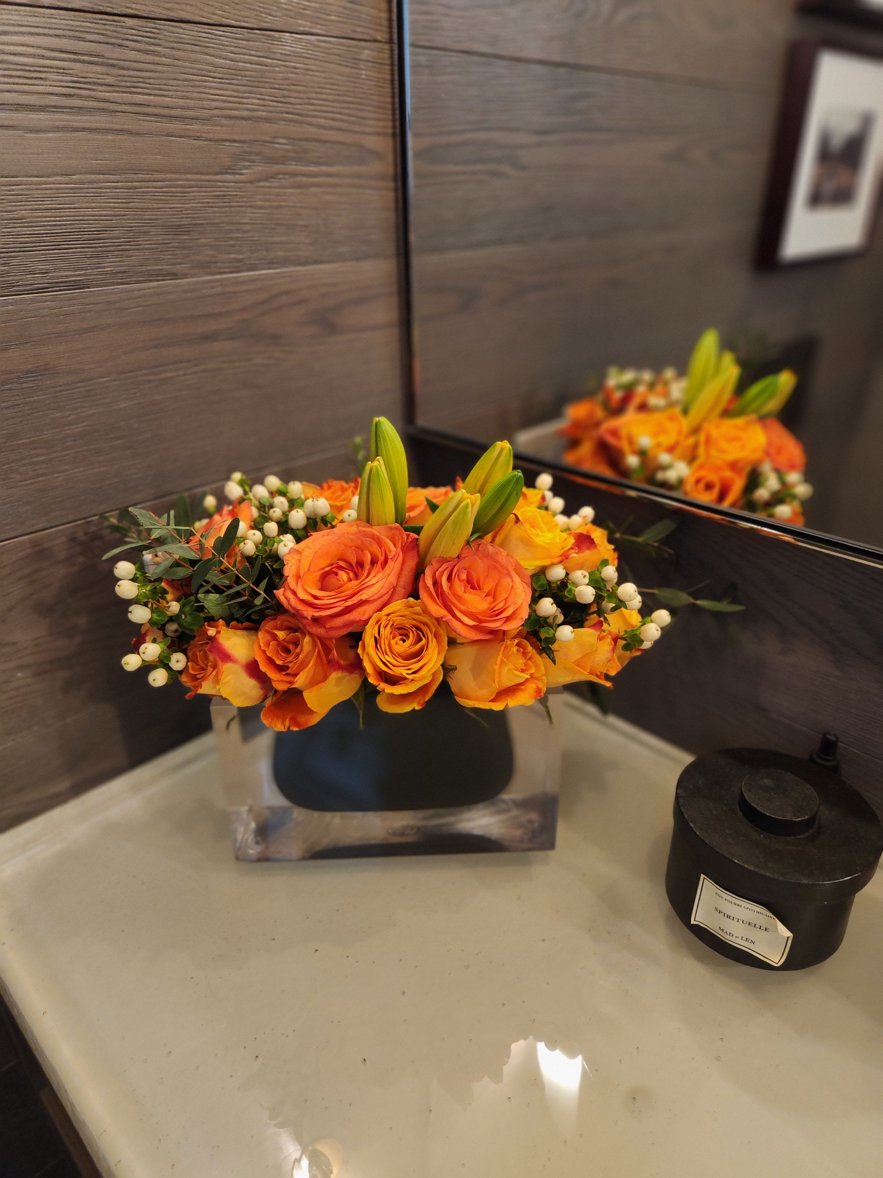 Orange roses and lily buds arranged in a low square vase