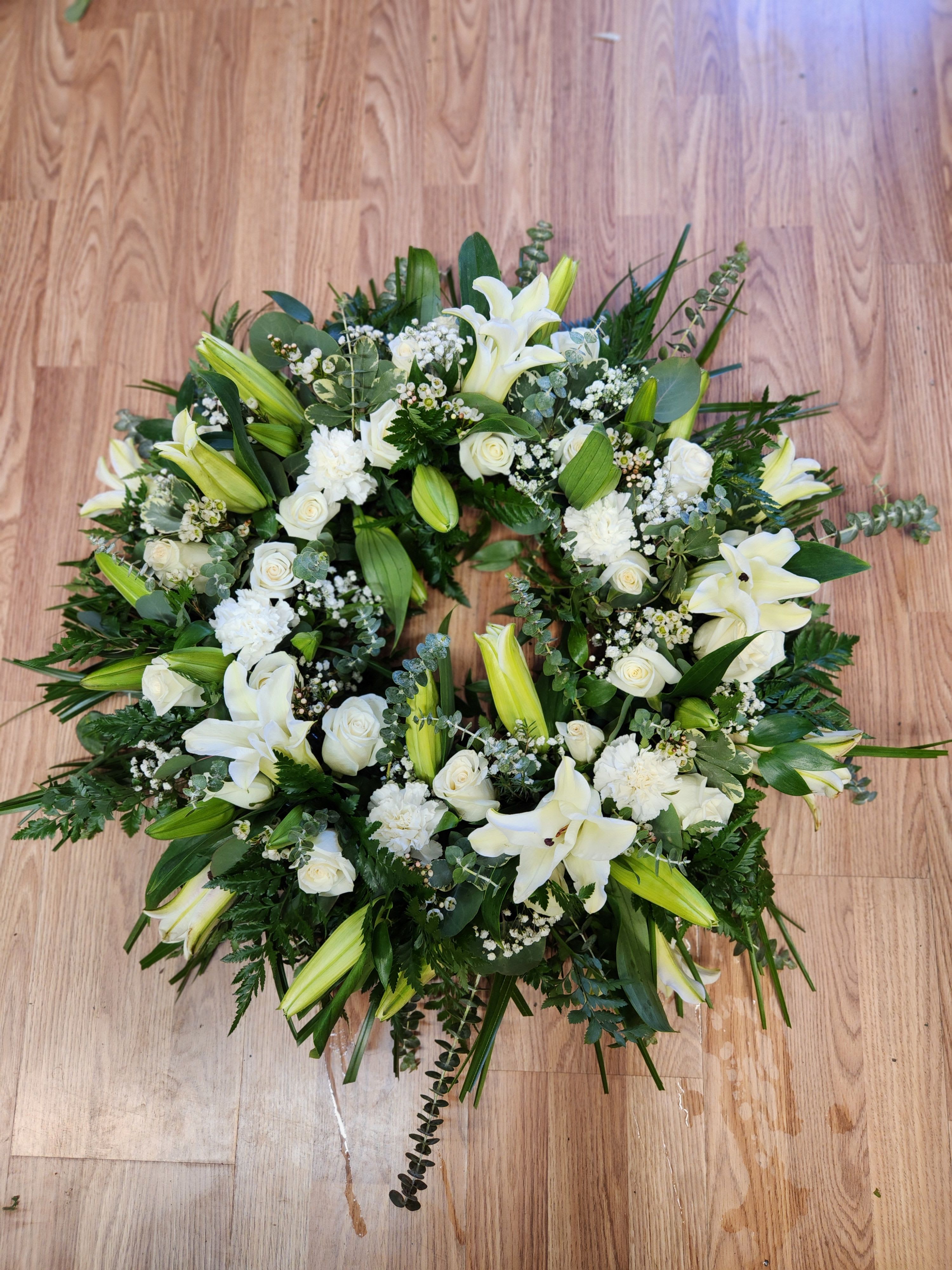 White floral wreath with lilies and roses on a wooden floor