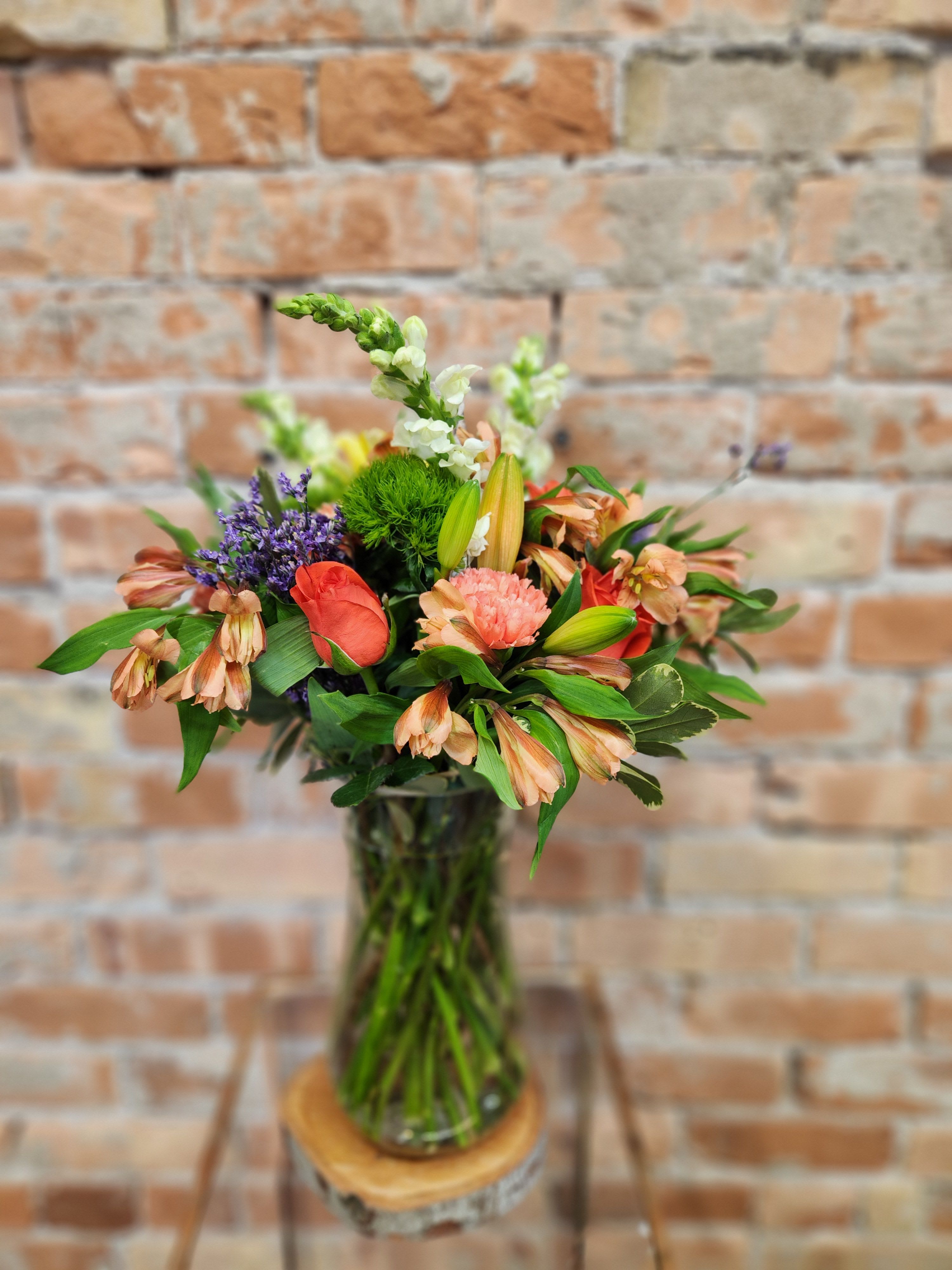 Mixed bouquet in a glass vase with coral, peach, purple, and white blooms