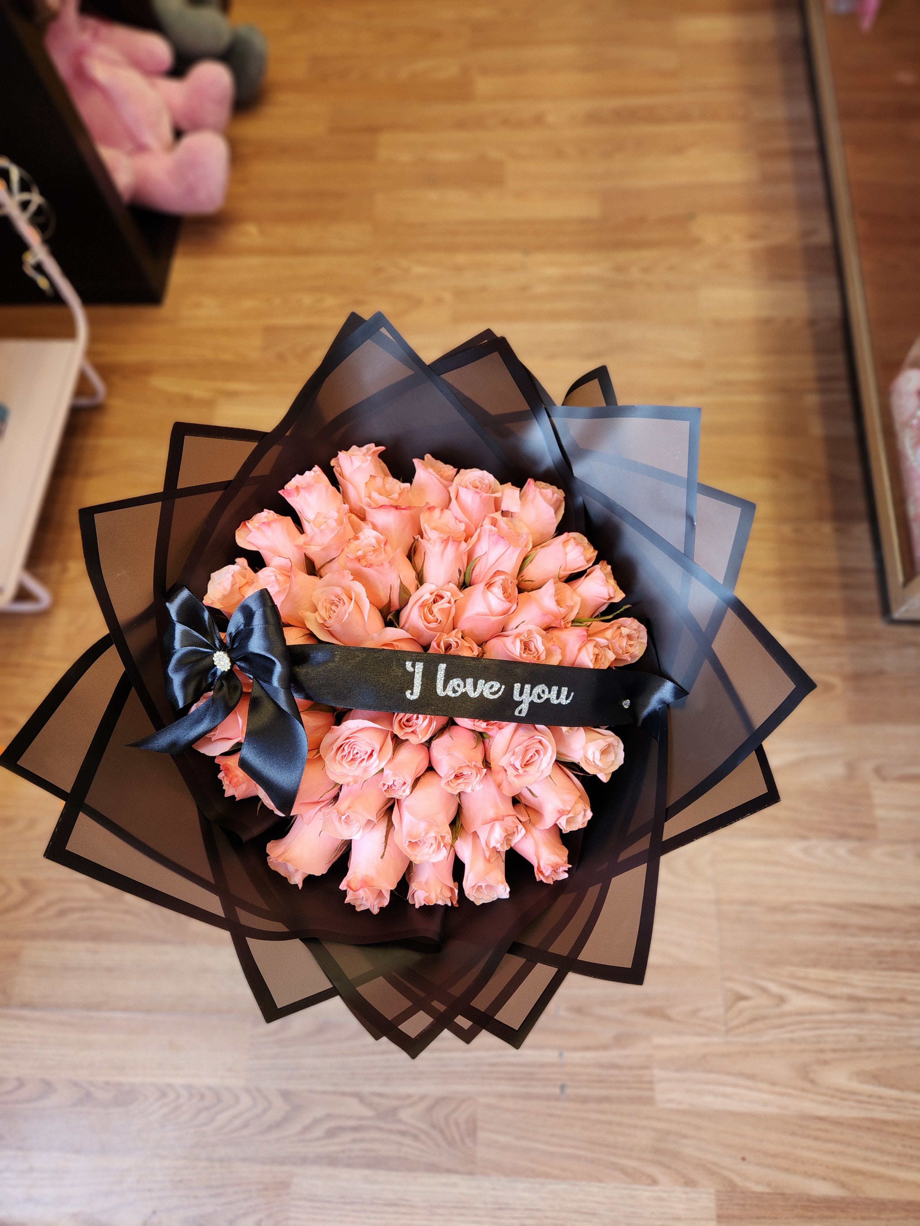 Bouquet of peach-pink roses wrapped in black paper with a ribbon