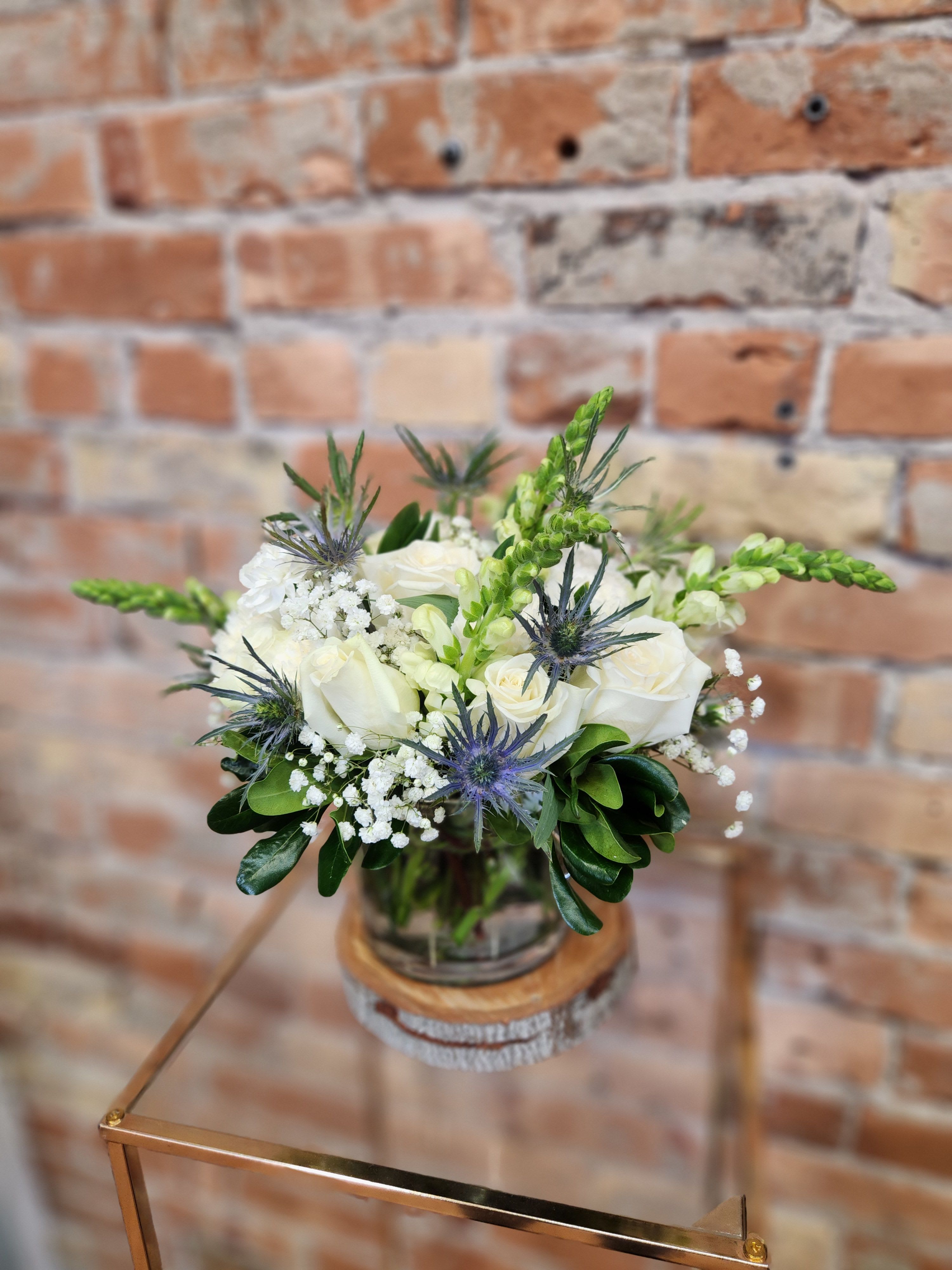 White rose bouquet with blue thistle in a glass vase