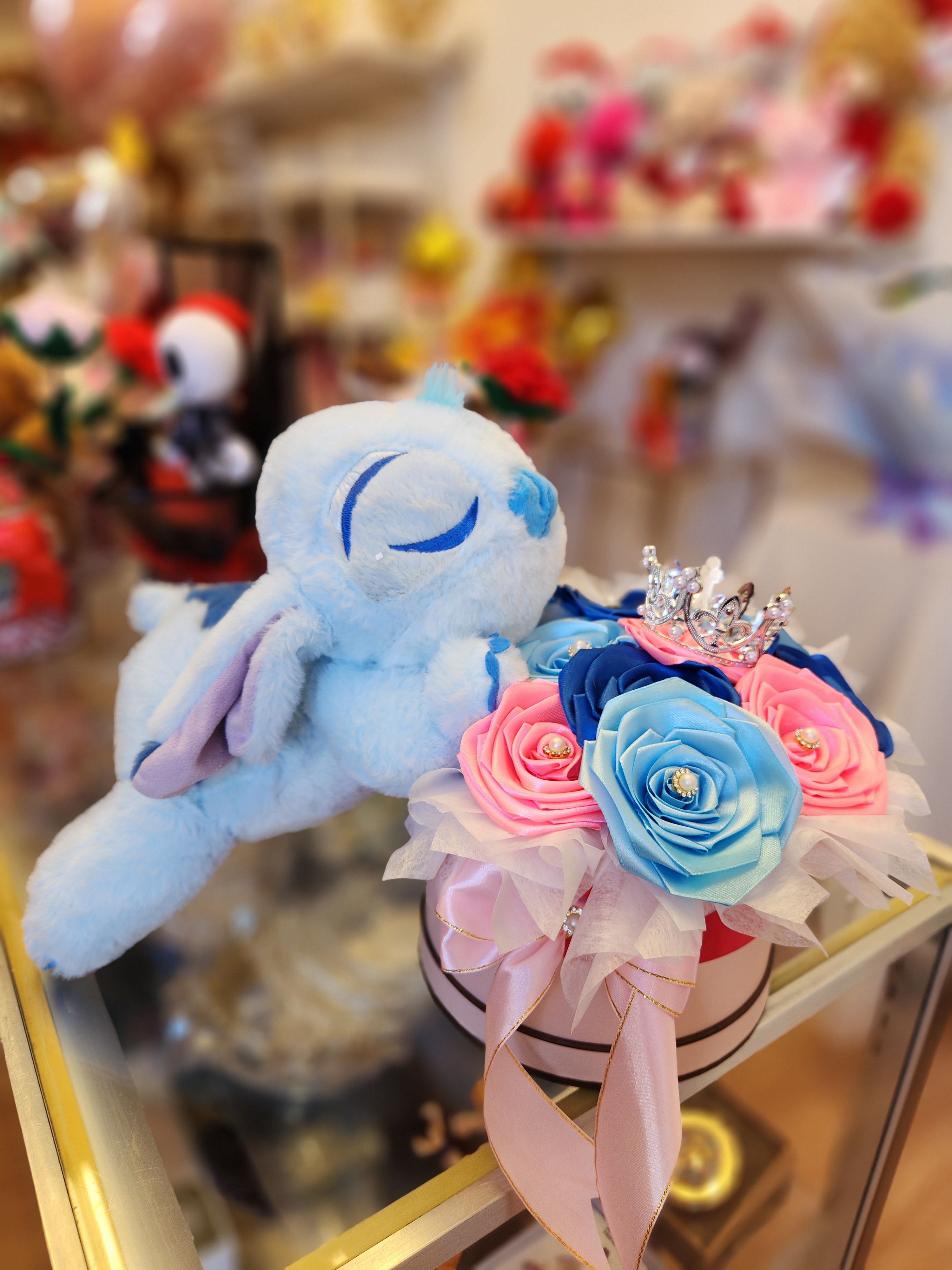 Plush bunny beside a box of blue and pink roses with a small crown