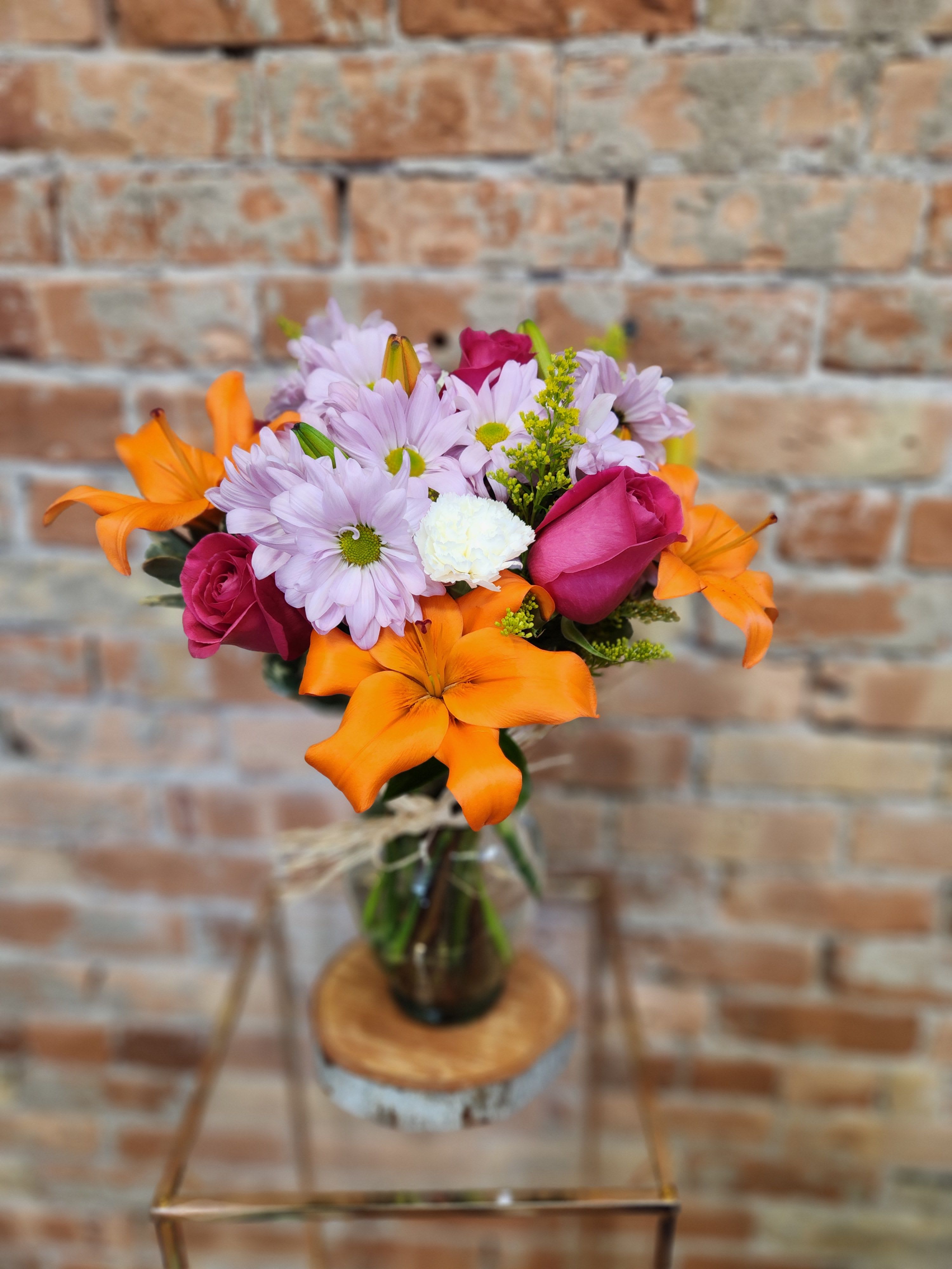 Bouquet of orange lilies, pink roses, and lavender daisies in a glass vase