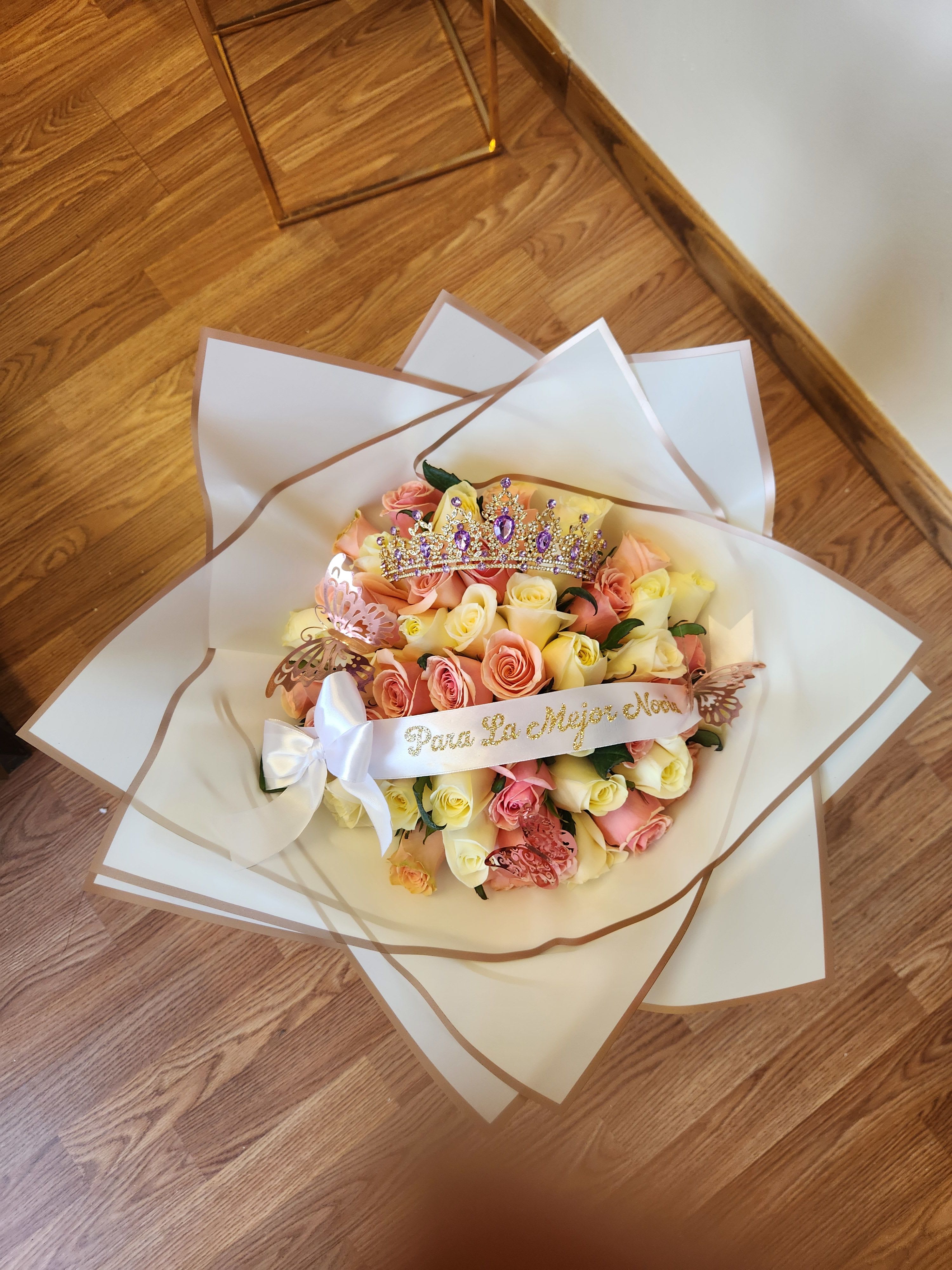 Bouquet of pink and yellow roses with a jeweled crown and ribbon