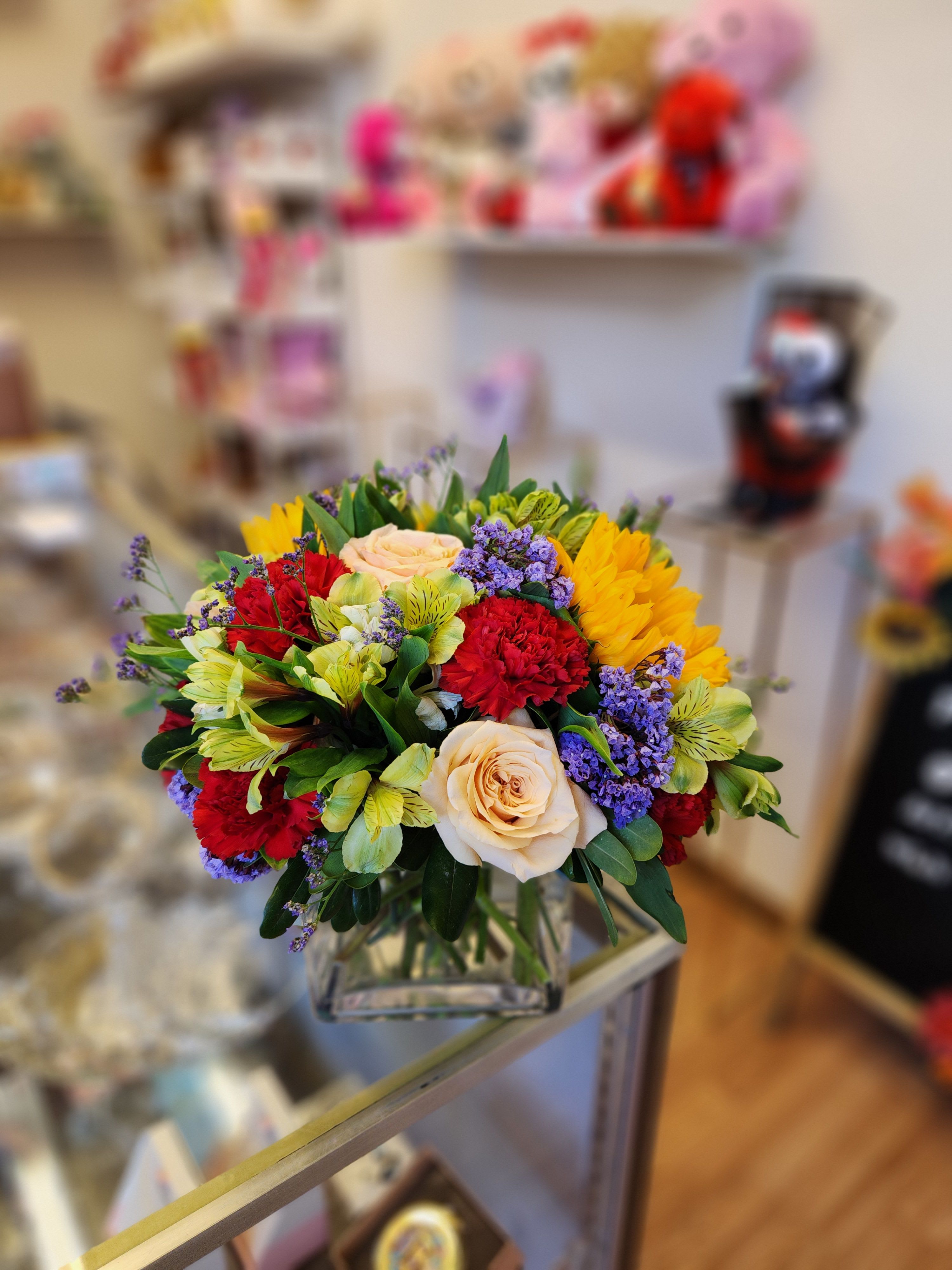 Mixed bouquet of roses, carnations, and purple filler in a glass vase