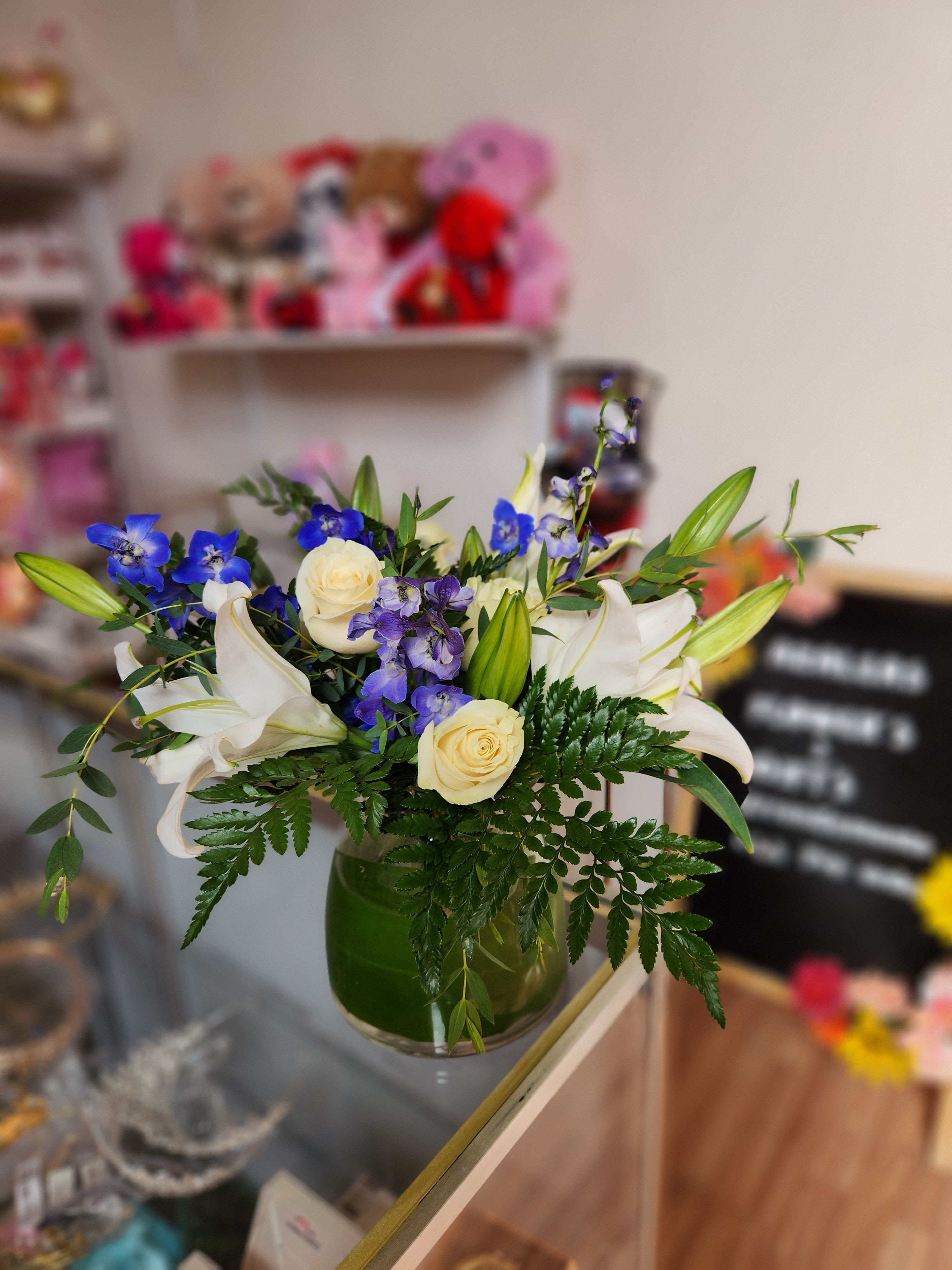 Bouquet of white lilies, cream roses, and blue flowers in a green glass vase