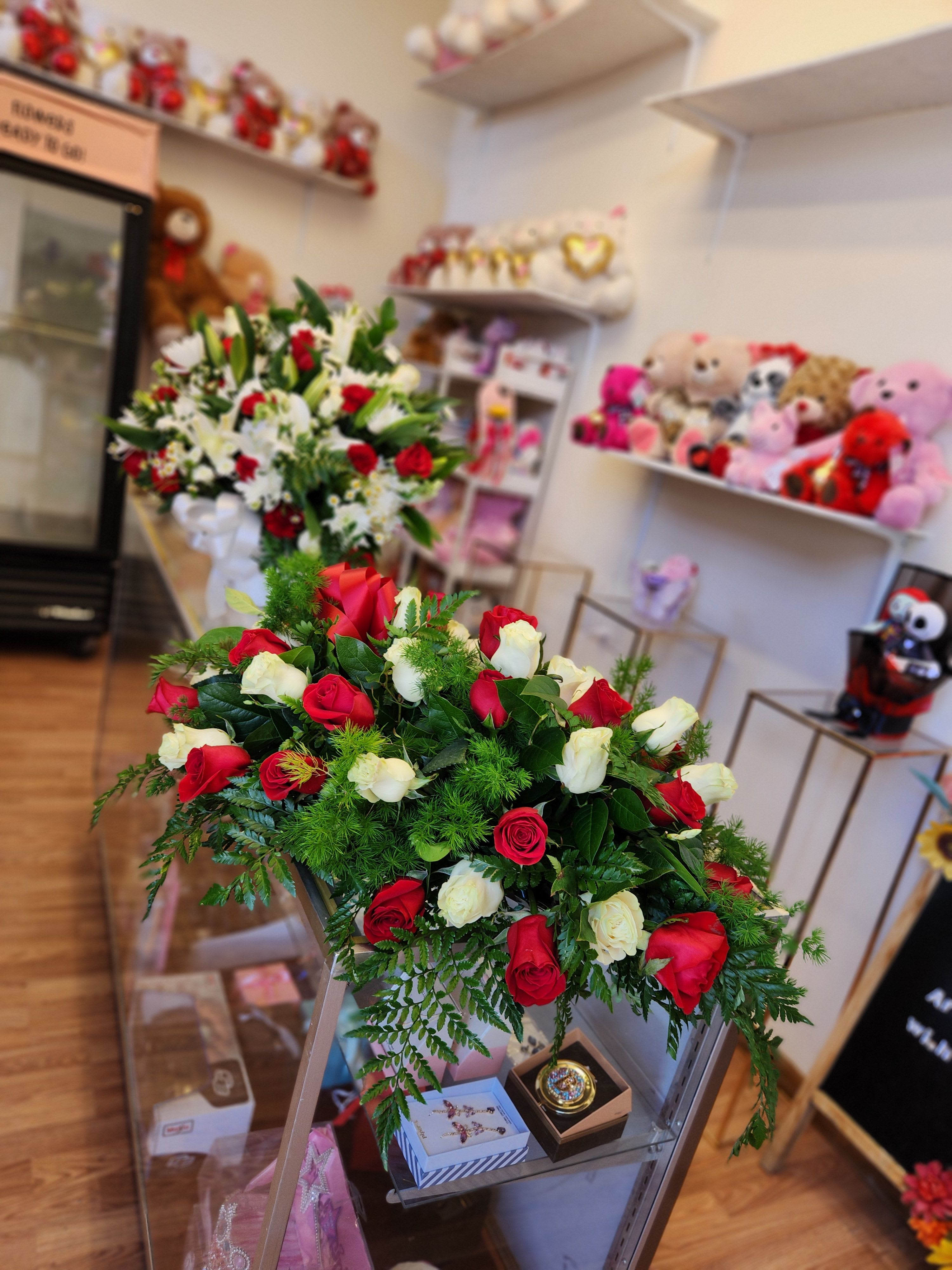 Two rose arrangements in a shop, one red and white bouquet in front and one mixed bouquet behind.