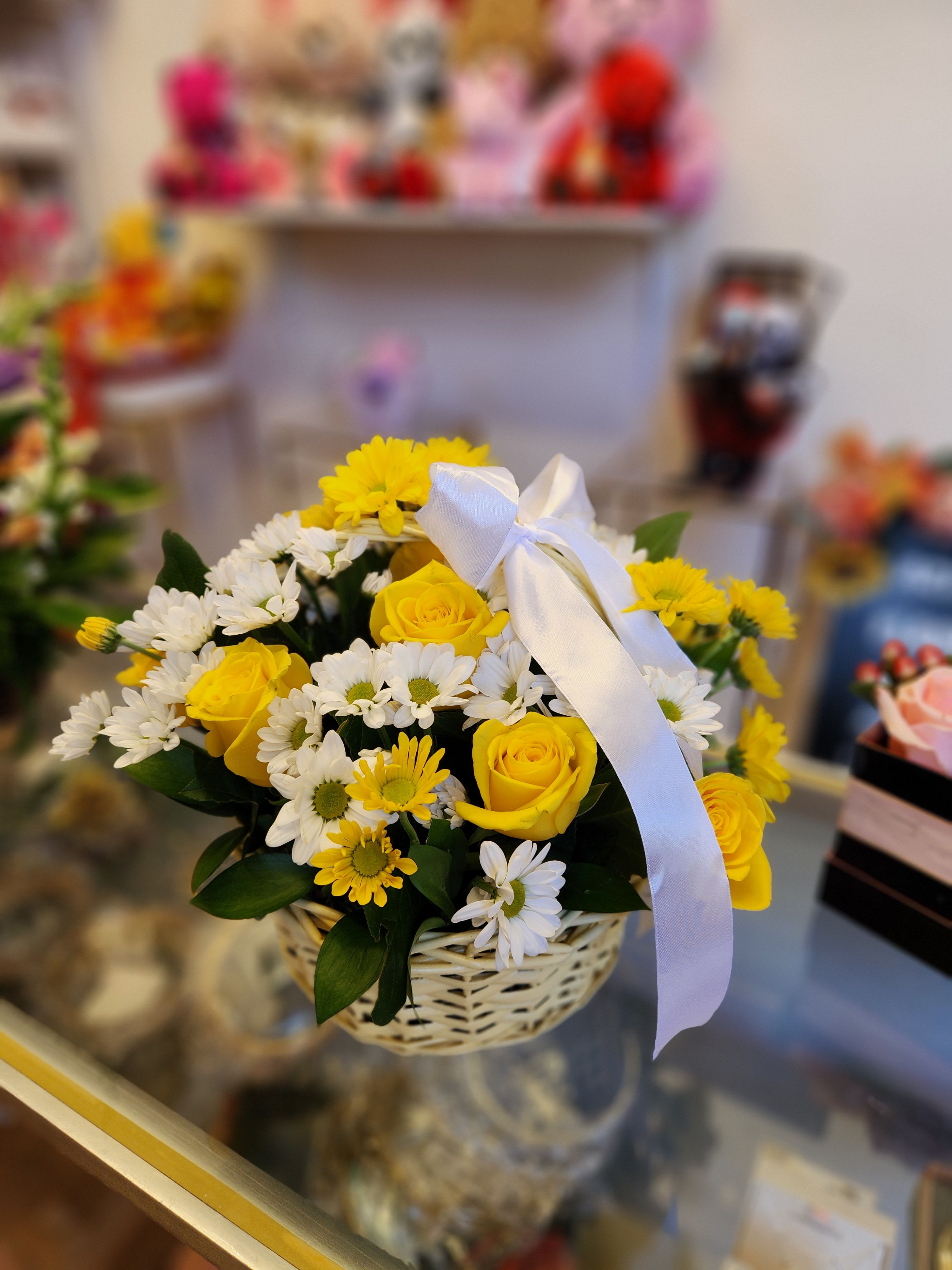 Yellow roses and white daisies in a wicker basket with a white ribbon
