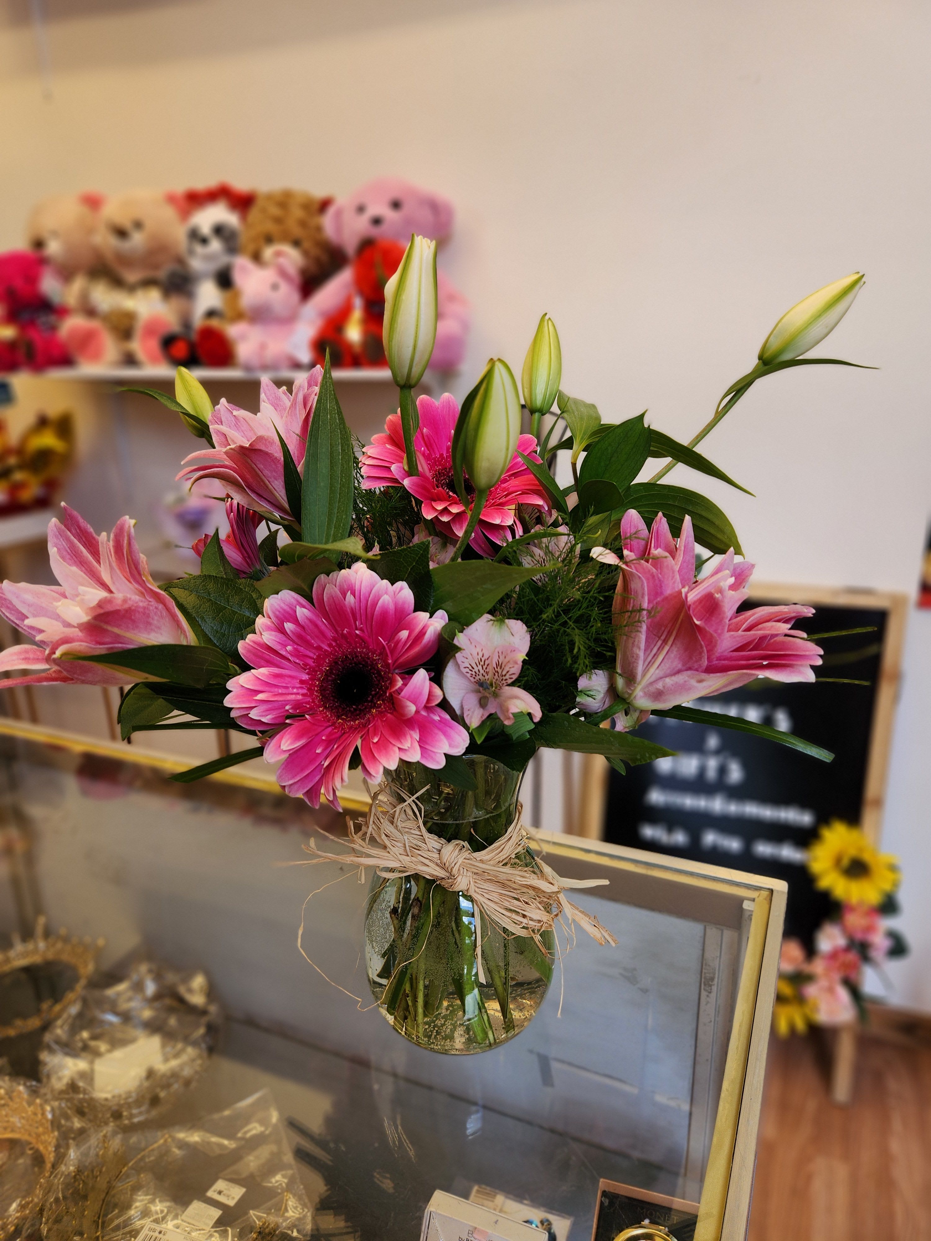 Pink gerbera daisies and lilies in a glass vase with raffia tie