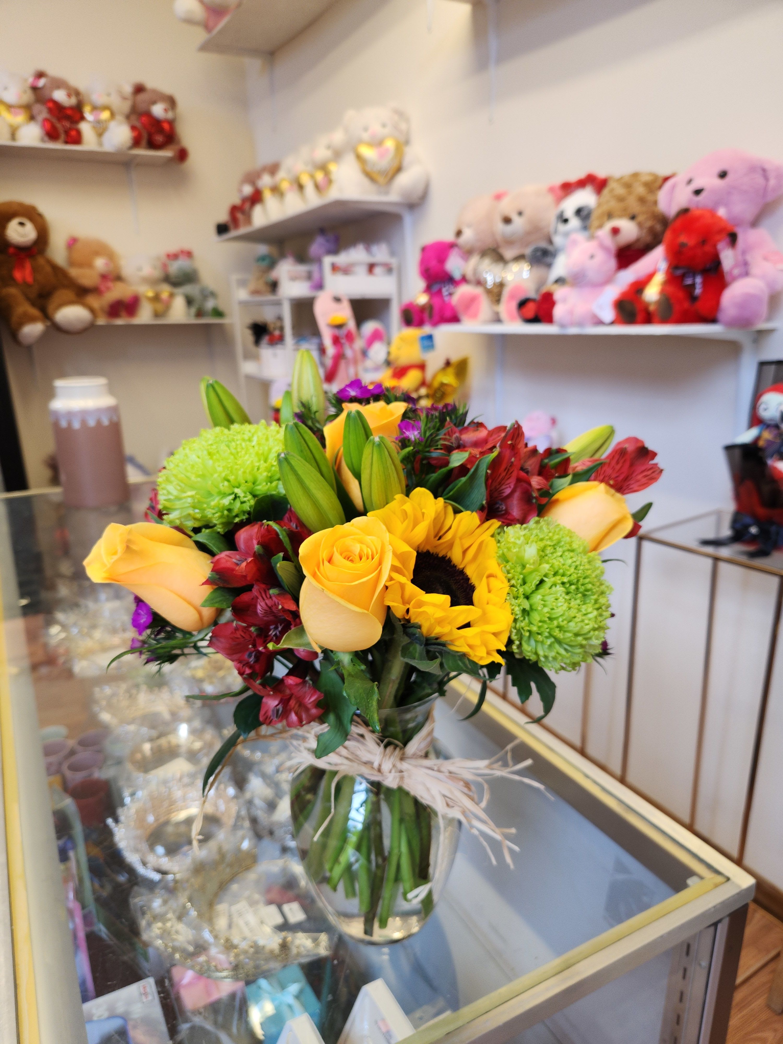 Bouquet of yellow roses, sunflowers, and green chrysanthemums in a glass vase