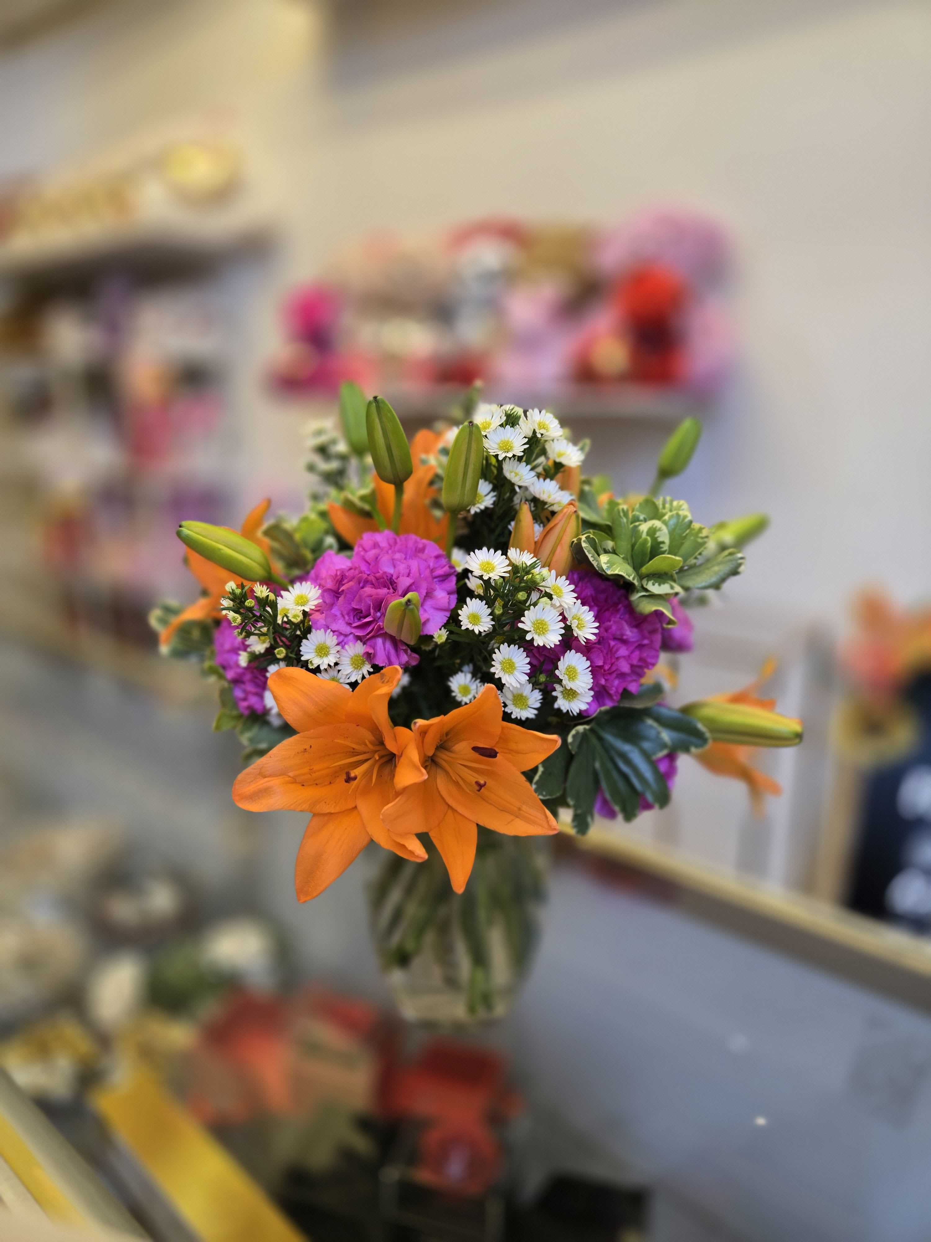 Bouquet of orange lilies, purple flowers, and white daisies in a glass vase