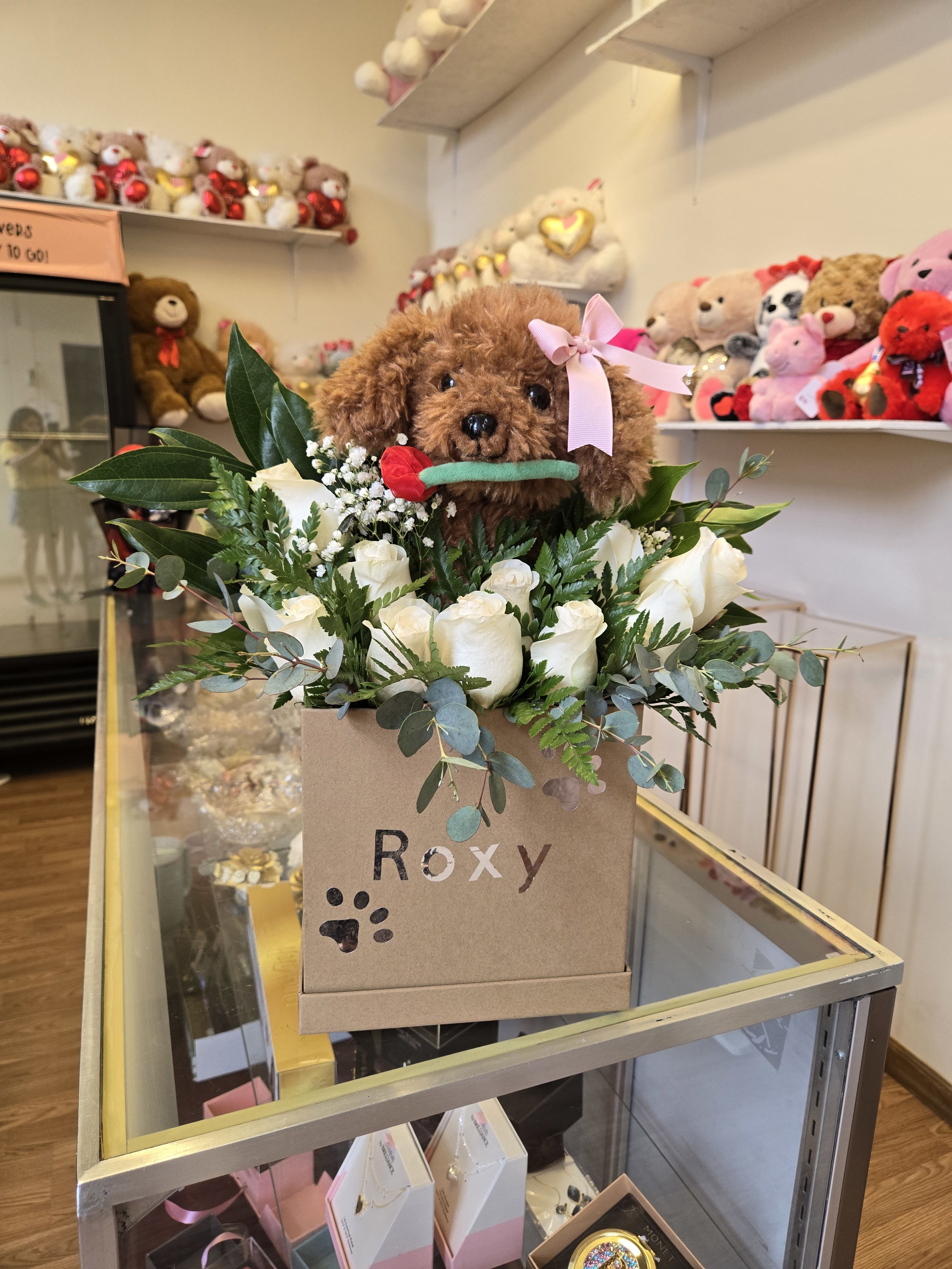 White roses and greenery in a gift box with a teddy bear on top
