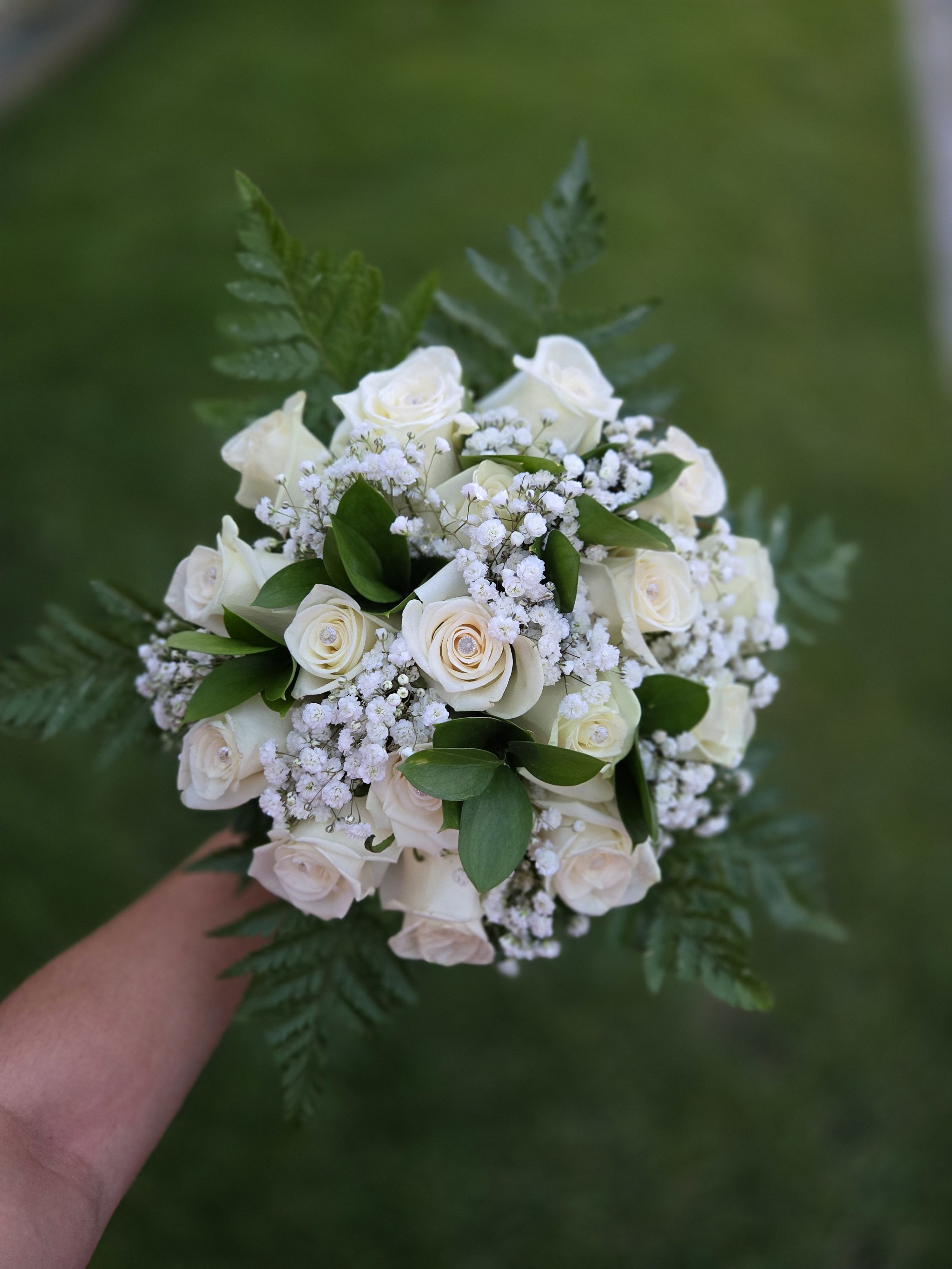 Handheld bouquet of white roses with baby's breath and greenery