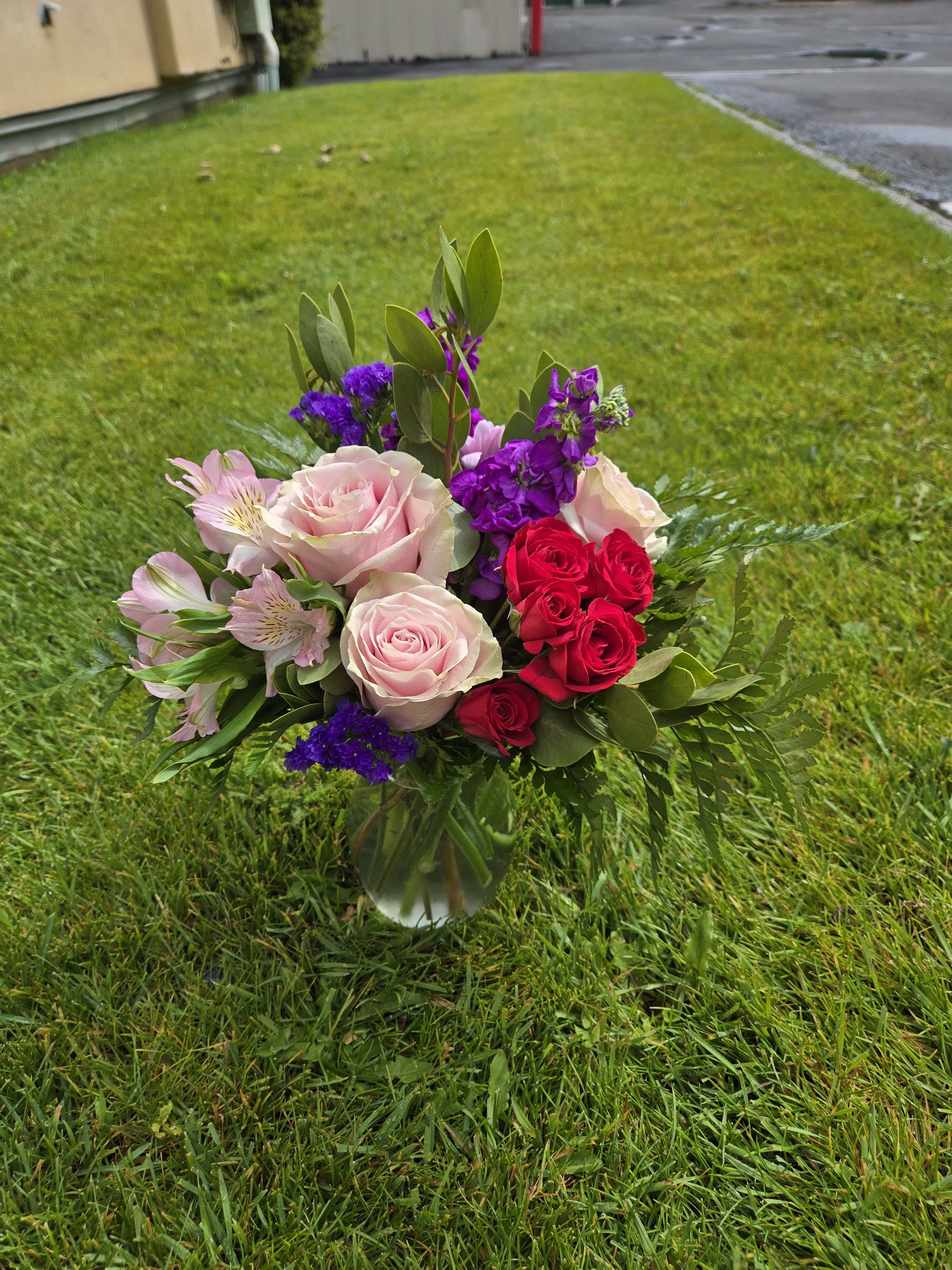 Bouquet of pink and red roses with purple accents in a glass vase