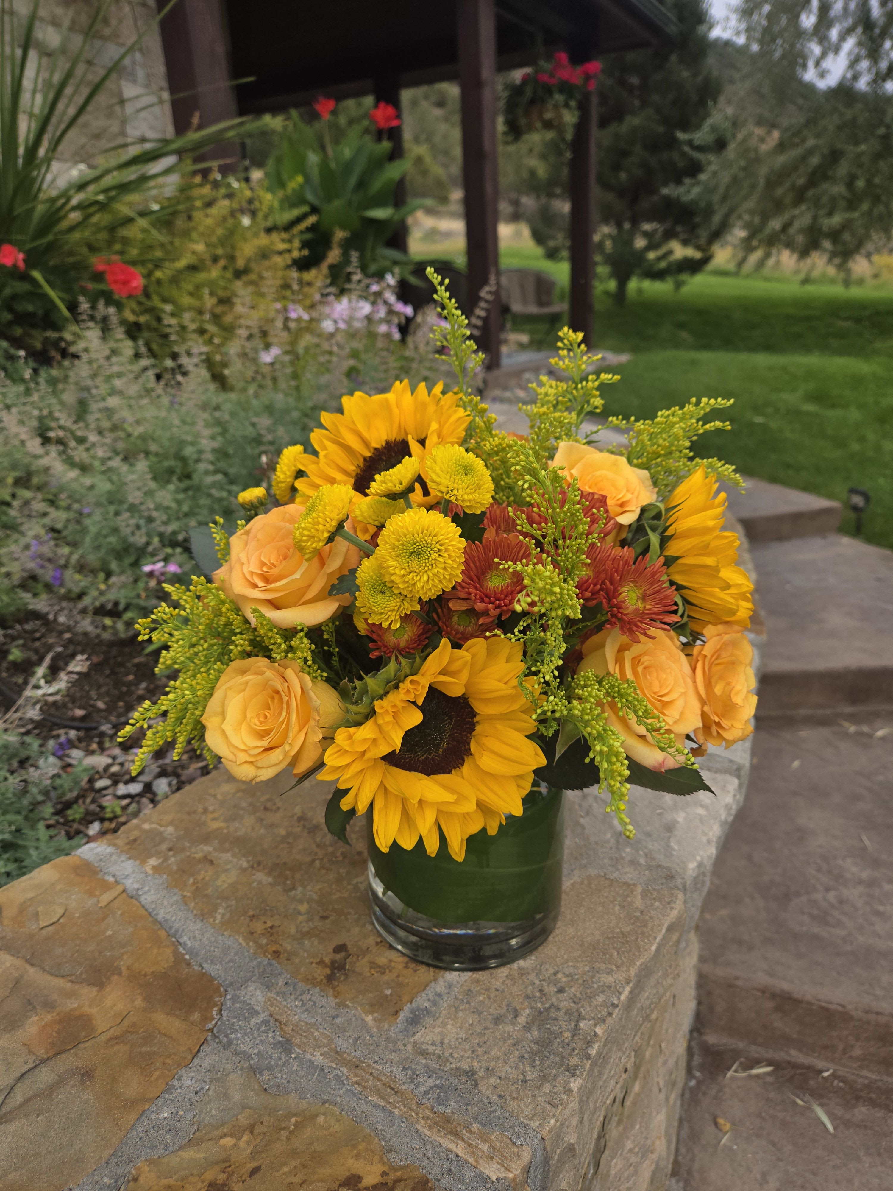 Bouquet of sunflowers, yellow roses, and mums in a glass vase