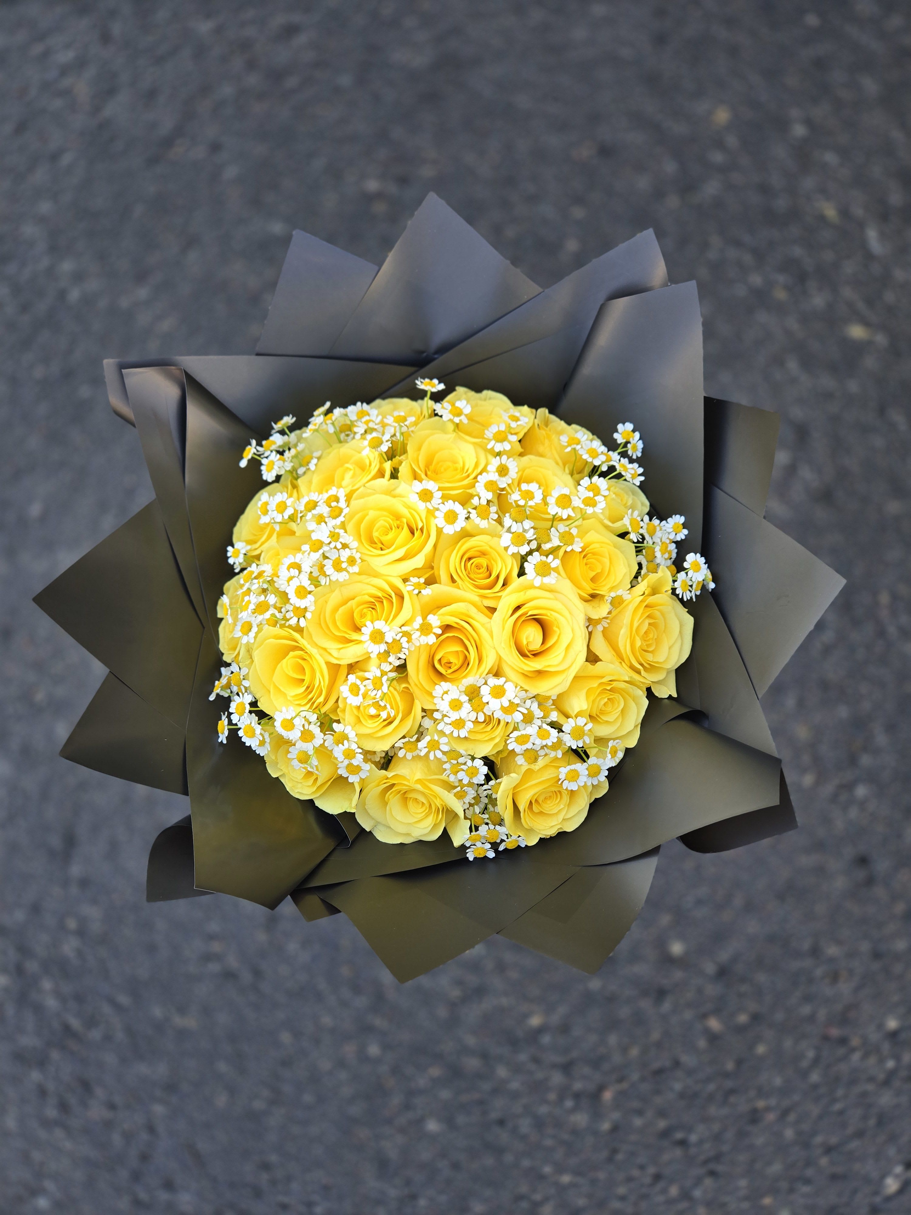 Bouquet of yellow roses with small white daisies in dark wrapping