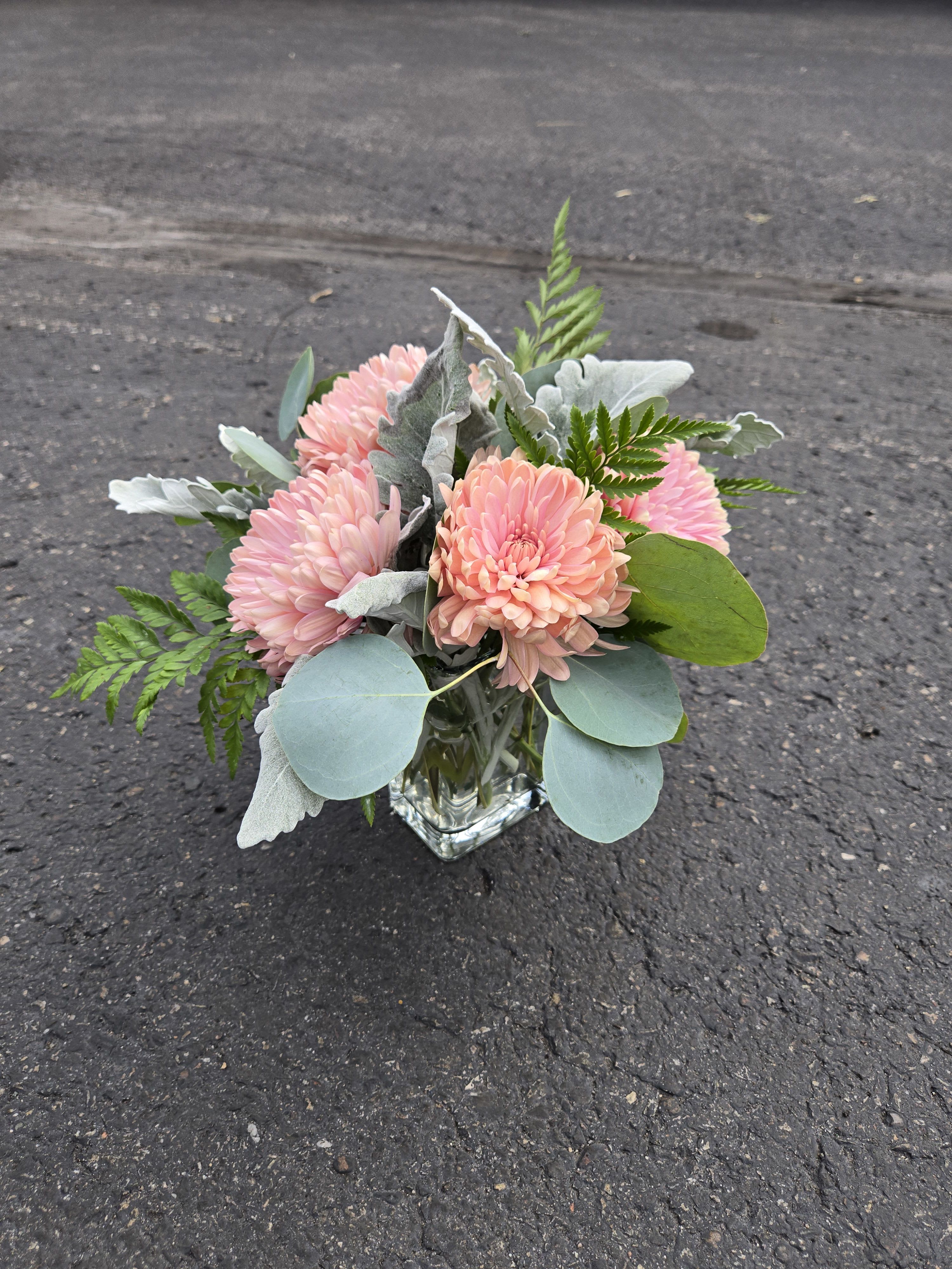 Pink chrysanthemum bouquet in a clear square vase with silver foliage